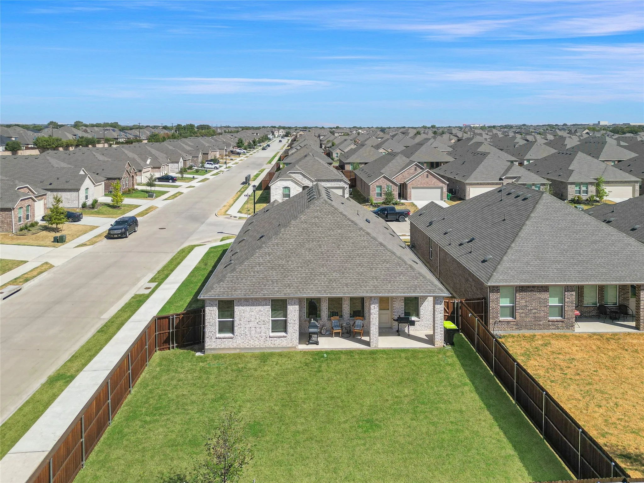 Expansive backyard with a manicured lawn, full privacy fencing, and a covered patio area