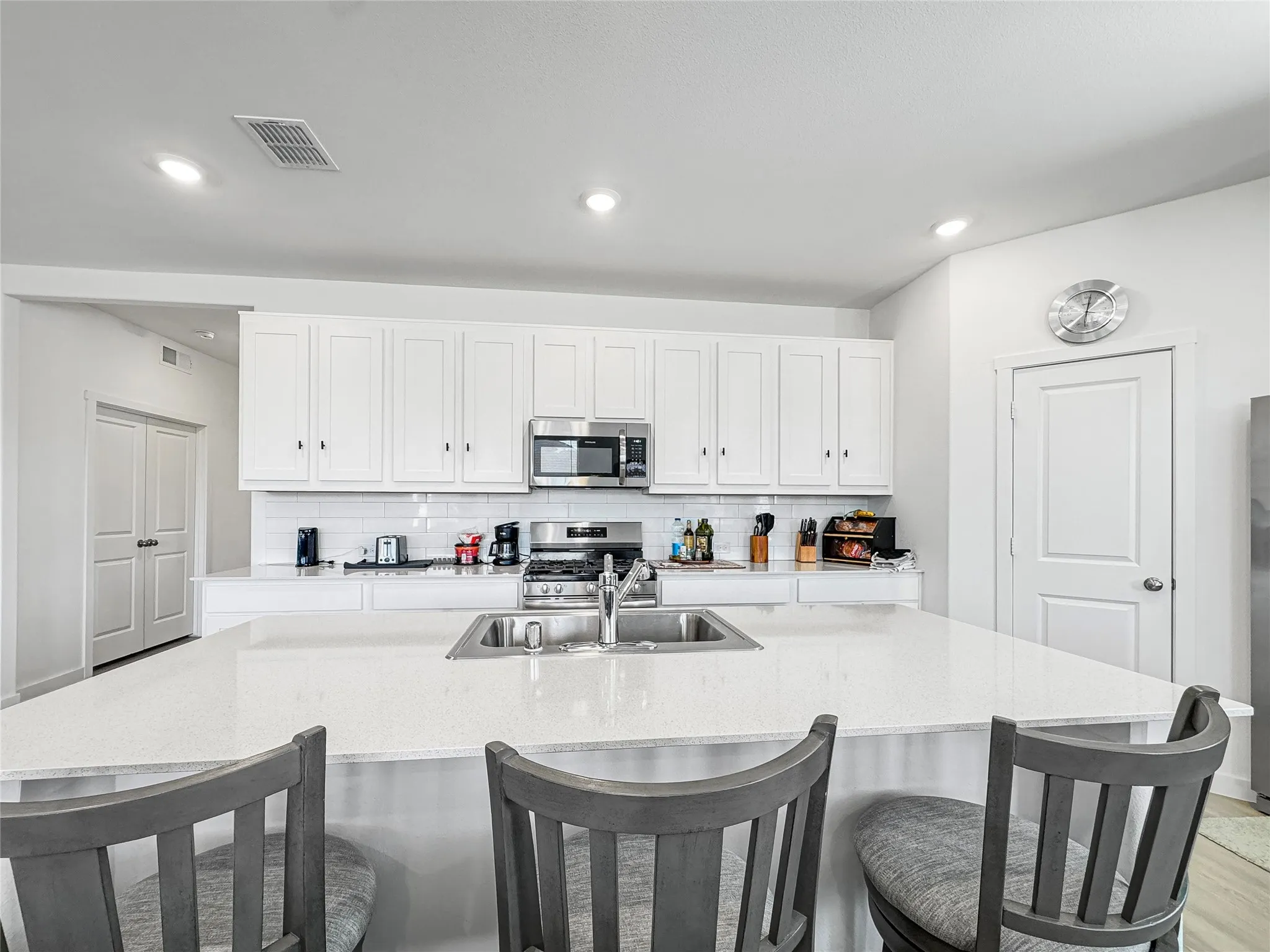 Kitchen featuring white cabinetry, stainless steel appliances, a white subway tile backsplash, recessed lighting, and an expansive island with an integrated sink