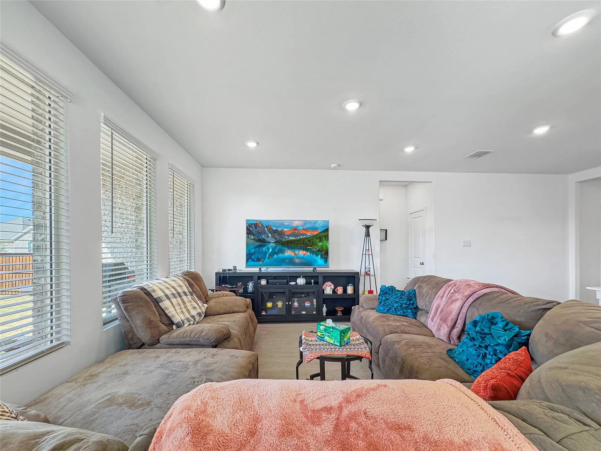 Recessed lighting, multiple windows, window blinds, white walls, wood-finish flooring