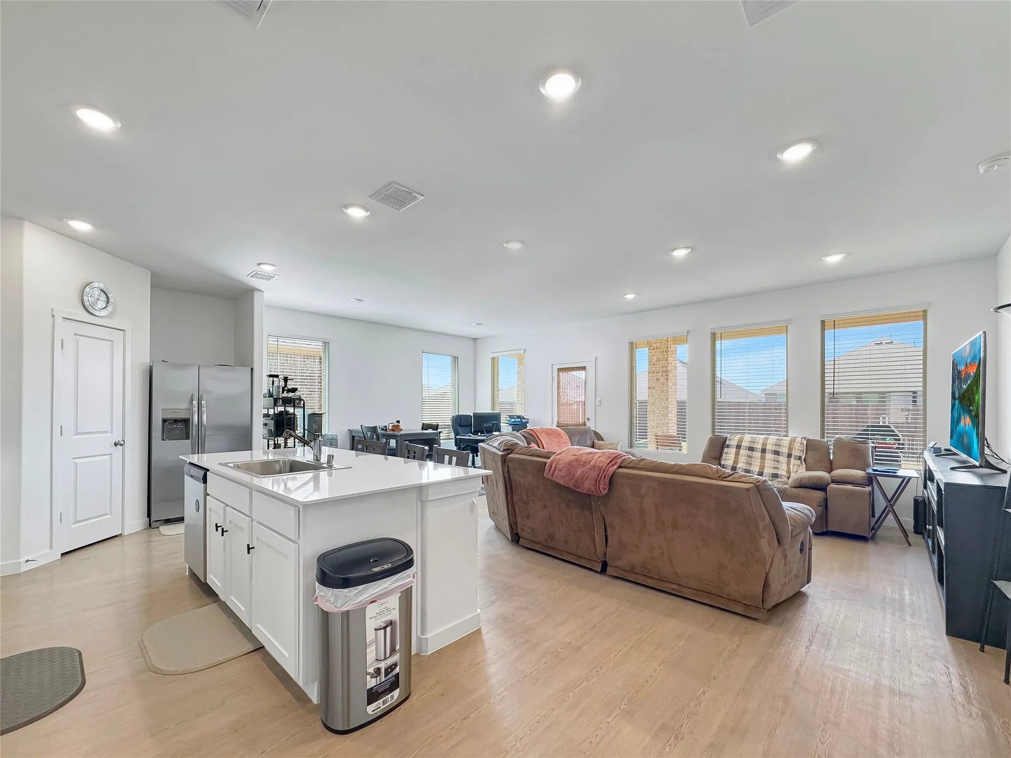 Open-concept living space featuring wood-finish flooring, recessed lighting, a kitchen island with a white countertop, and multiple large windows