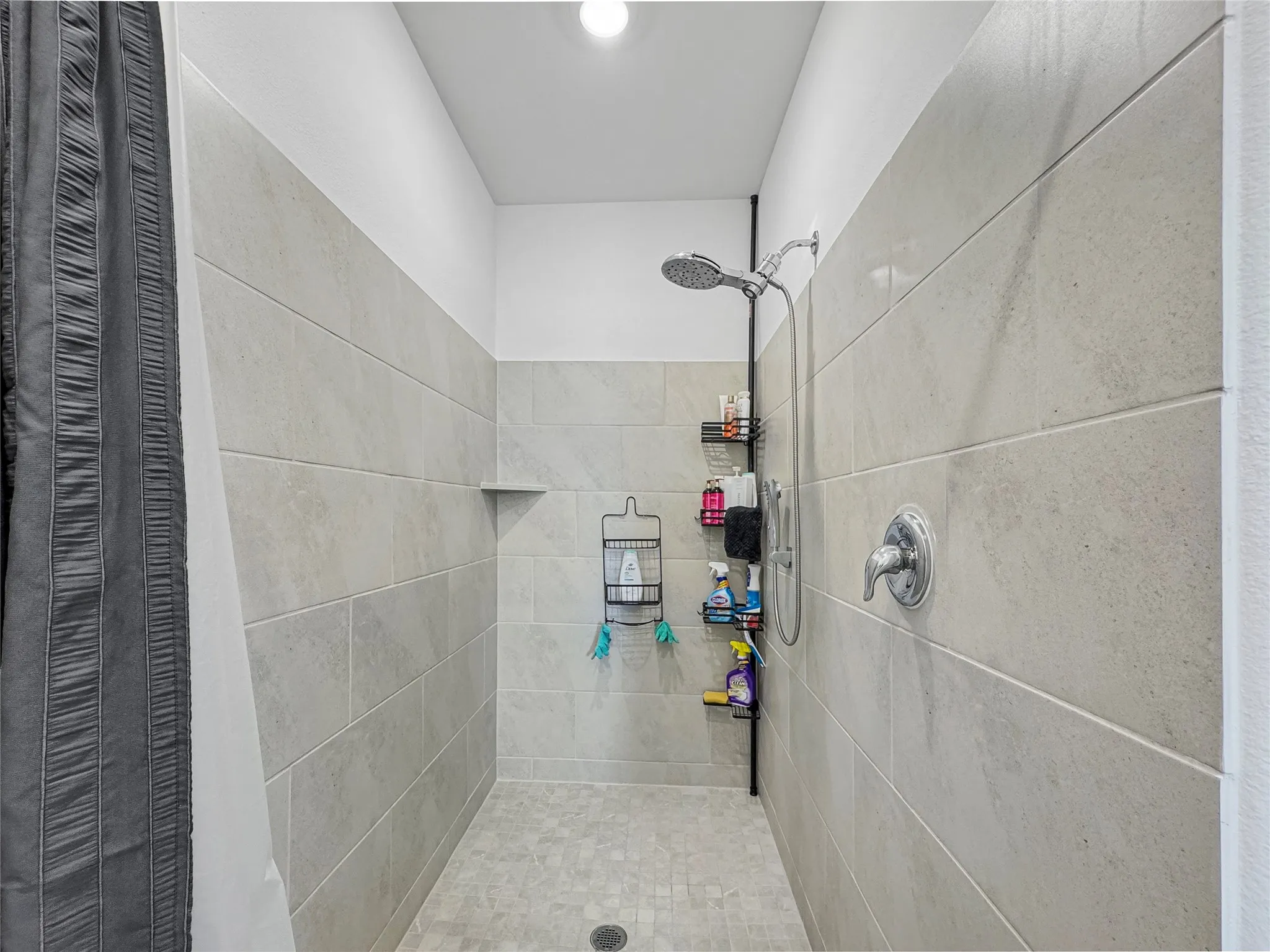 Tiled shower enclosure featuring light-toned rectangular wall tiles, a built-in corner shelf, and a handheld showerhead