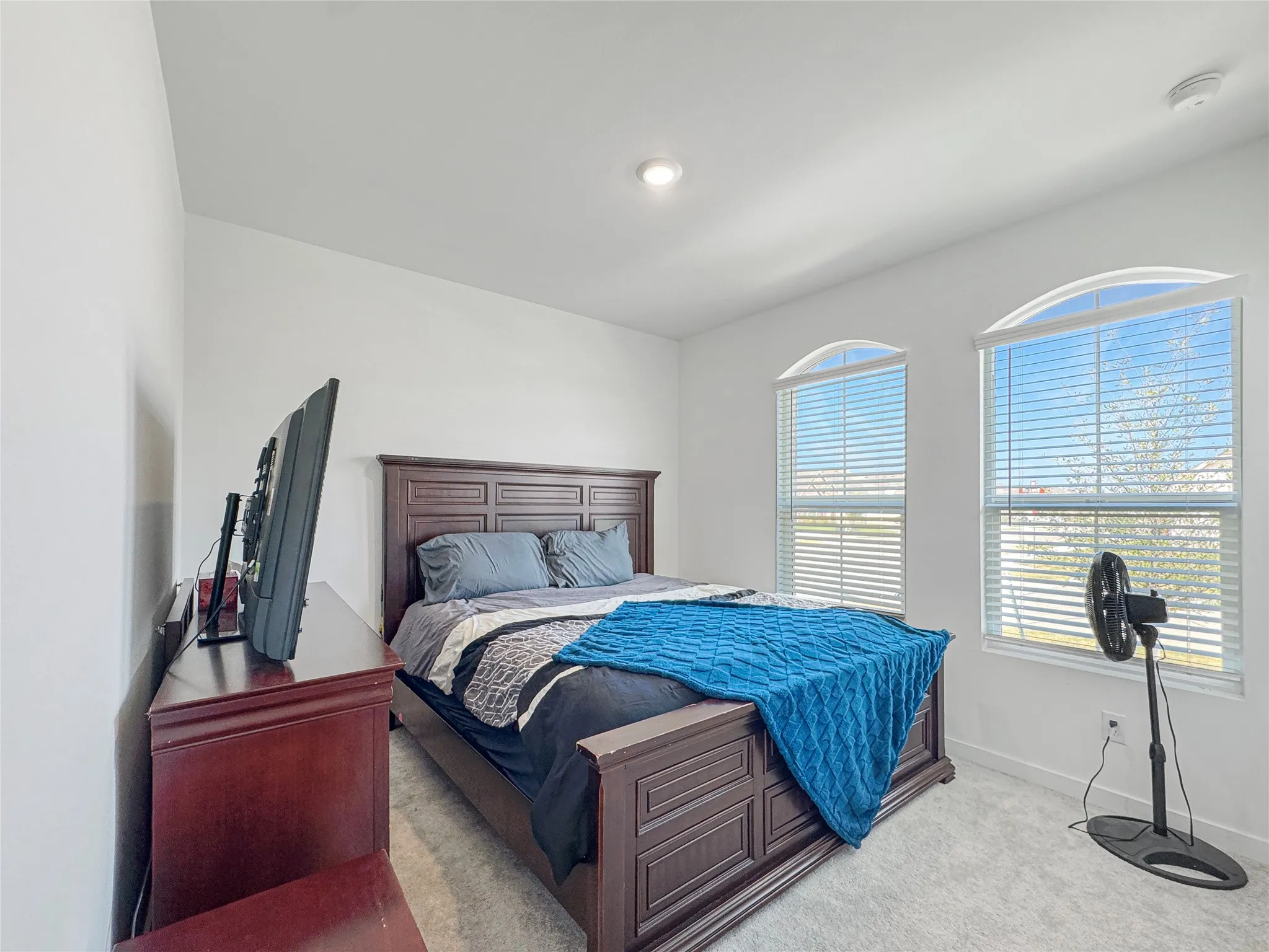 Recessed lighting illuminates a room featuring two arched windows, neutral wall paint, and gray carpet flooring