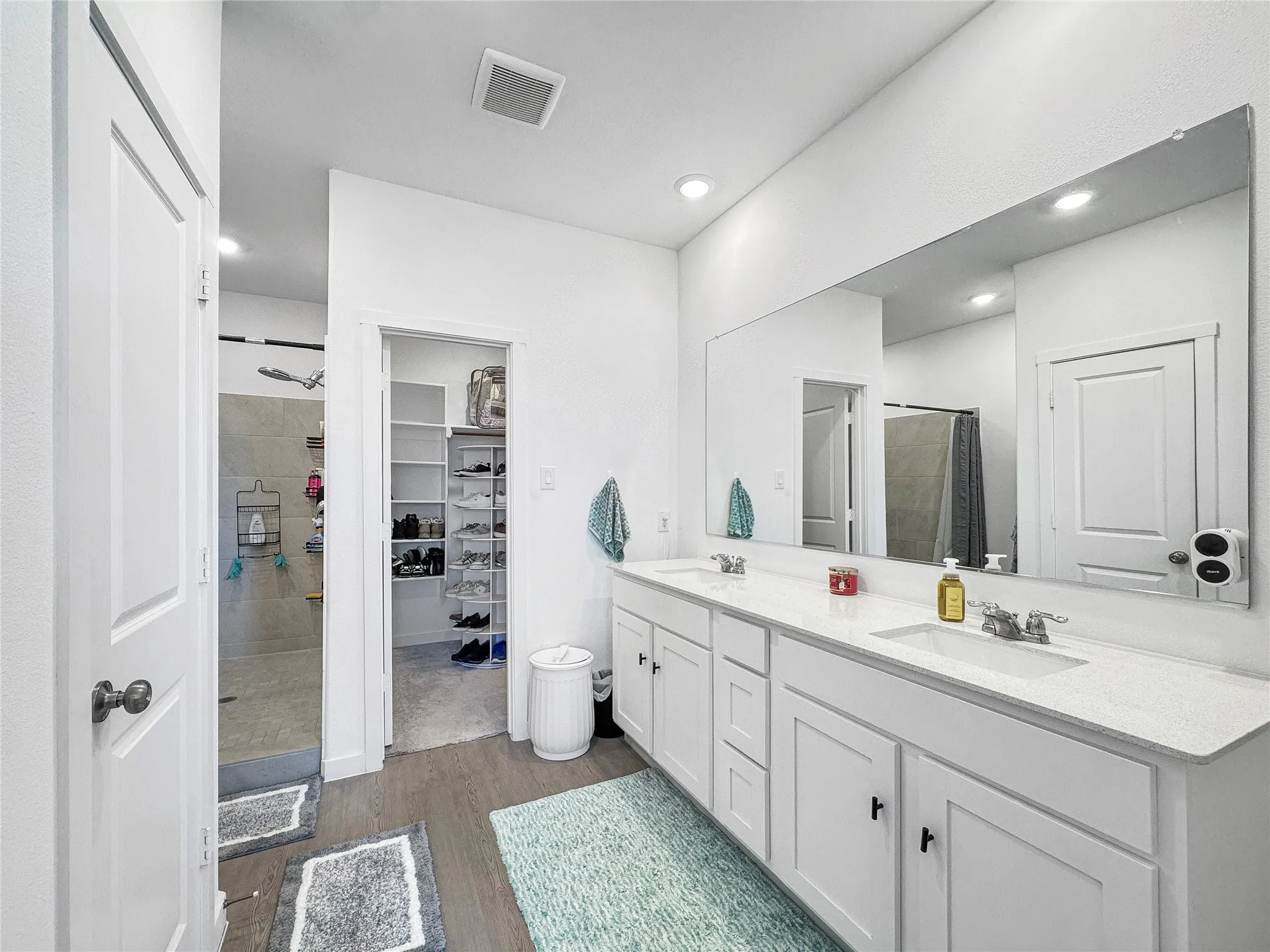 En suite bath with dual vanity with white cabinetry and integrated sinks, a wide mirror, recessed lighting, and wood-finish flooring