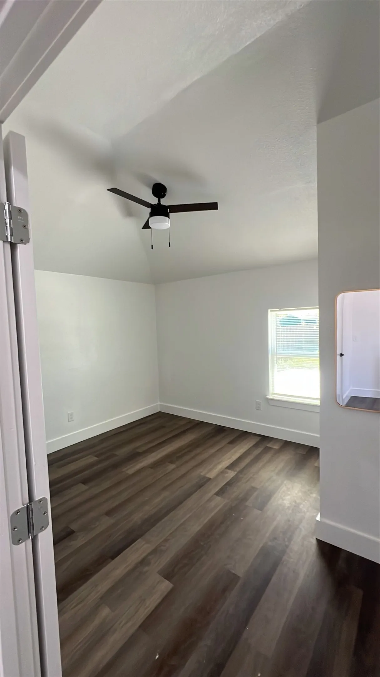 Wood-finish flooring with white baseboards, a ceiling fan with integrated lighting, and a window with white trim