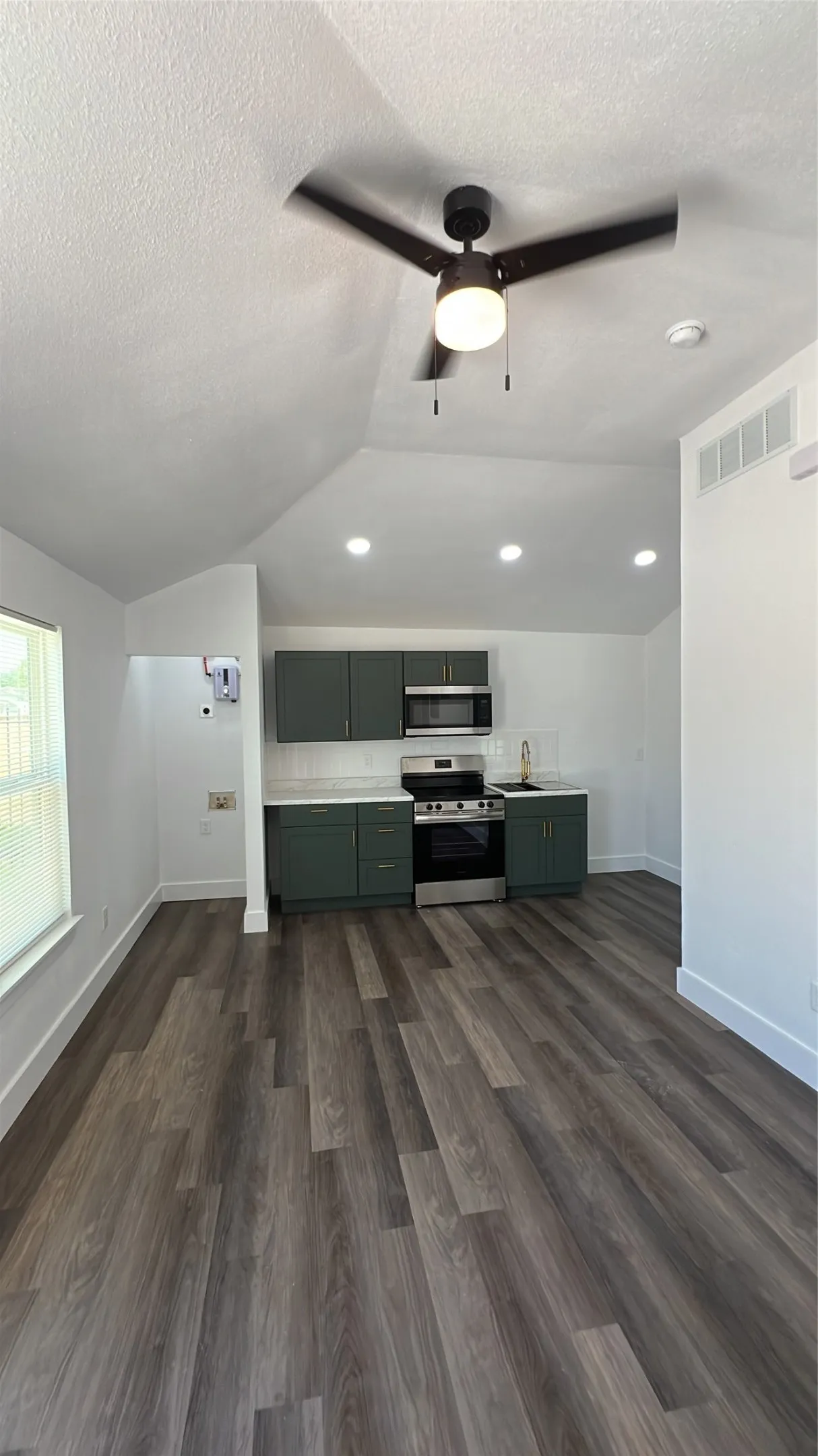 Vaulted ceiling with a ceiling fan, recessed lighting, wood-finish flooring, and a kitchen featuring dark green cabinetry with white countertops and a tiled backsplash