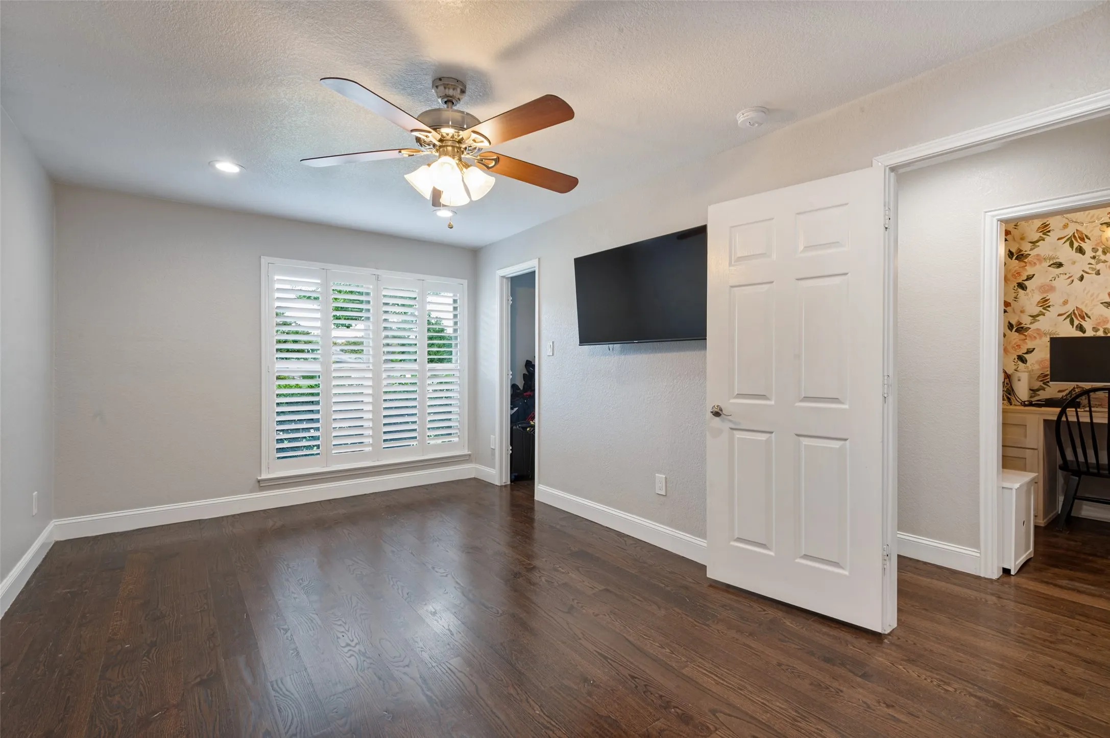 Wood flooring, white plantation shutters, and ceiling fan in bedroom