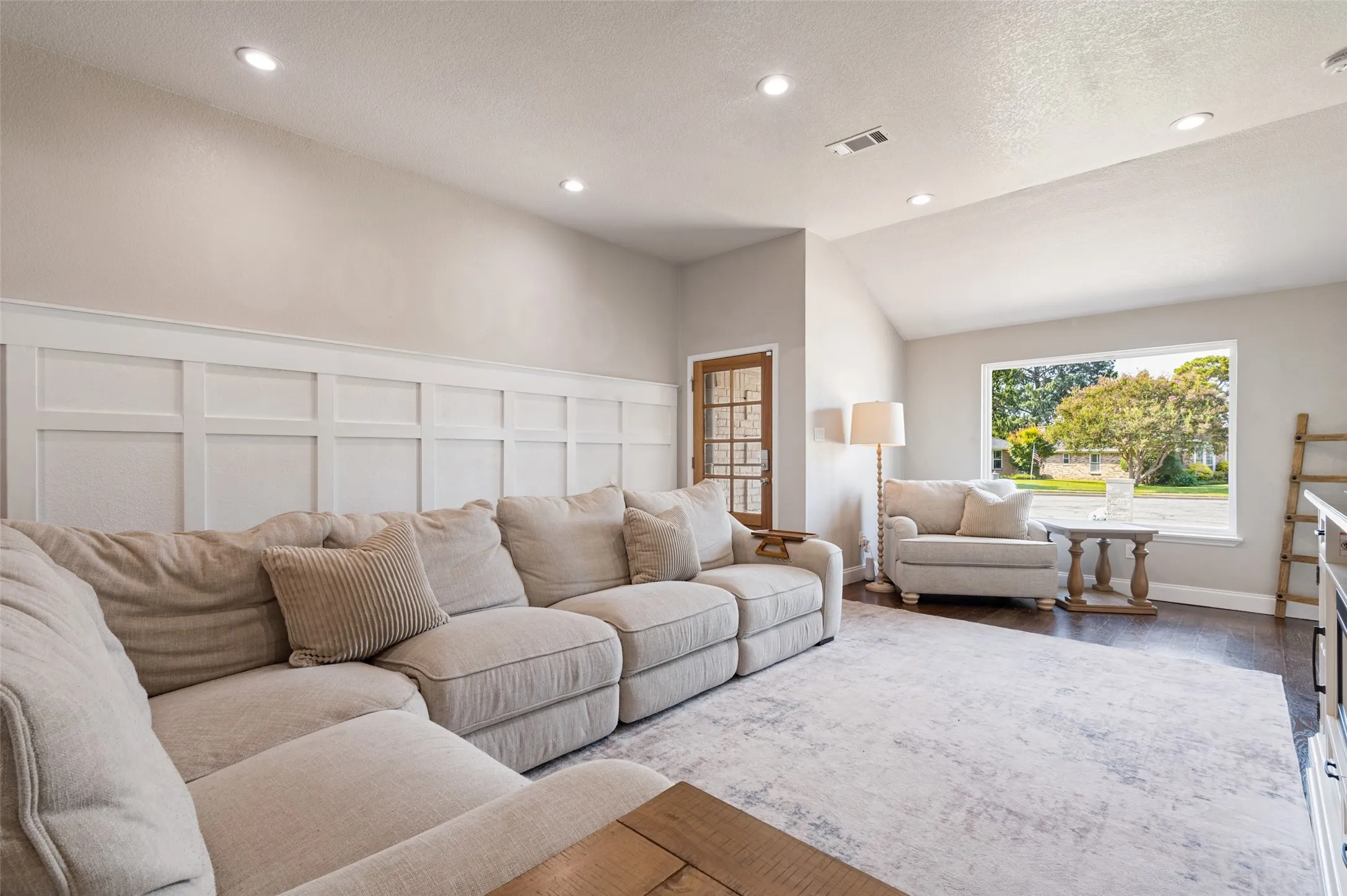 Spacious living area featuring board and batten wainscoting wall detailing, recessed lighting, and wood flooring