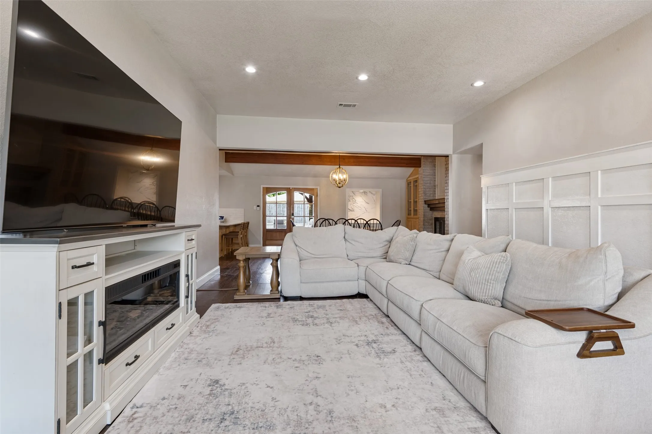 Recessed lighting in living room, white board and batten wainscoting paneling, wood flooring, exposed wood beams