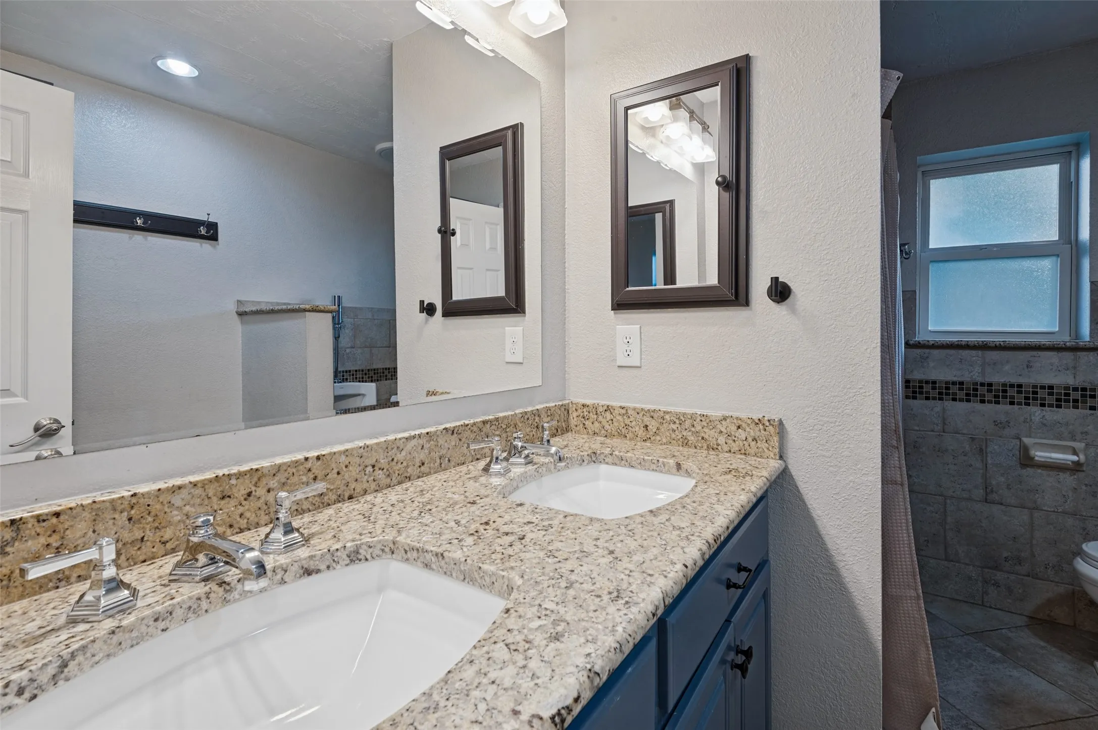 Dual undermount sinks with chrome fixtures in bathroom, granite countertop, dark blue vanity cabinetry