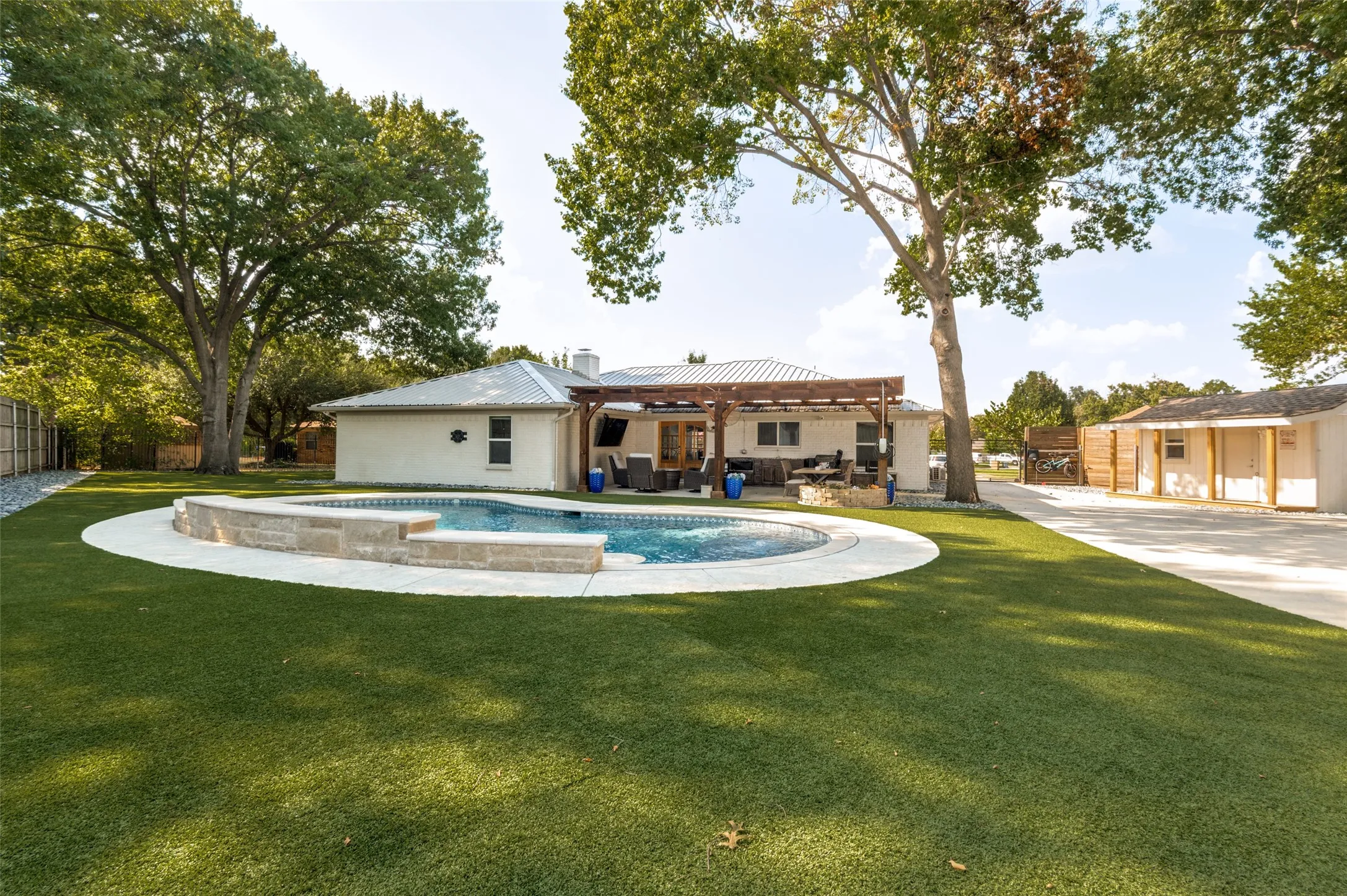 Expansive outdoor space featuring a swimming pool, a large patio with a wood pergola, and a detached structure with electricity