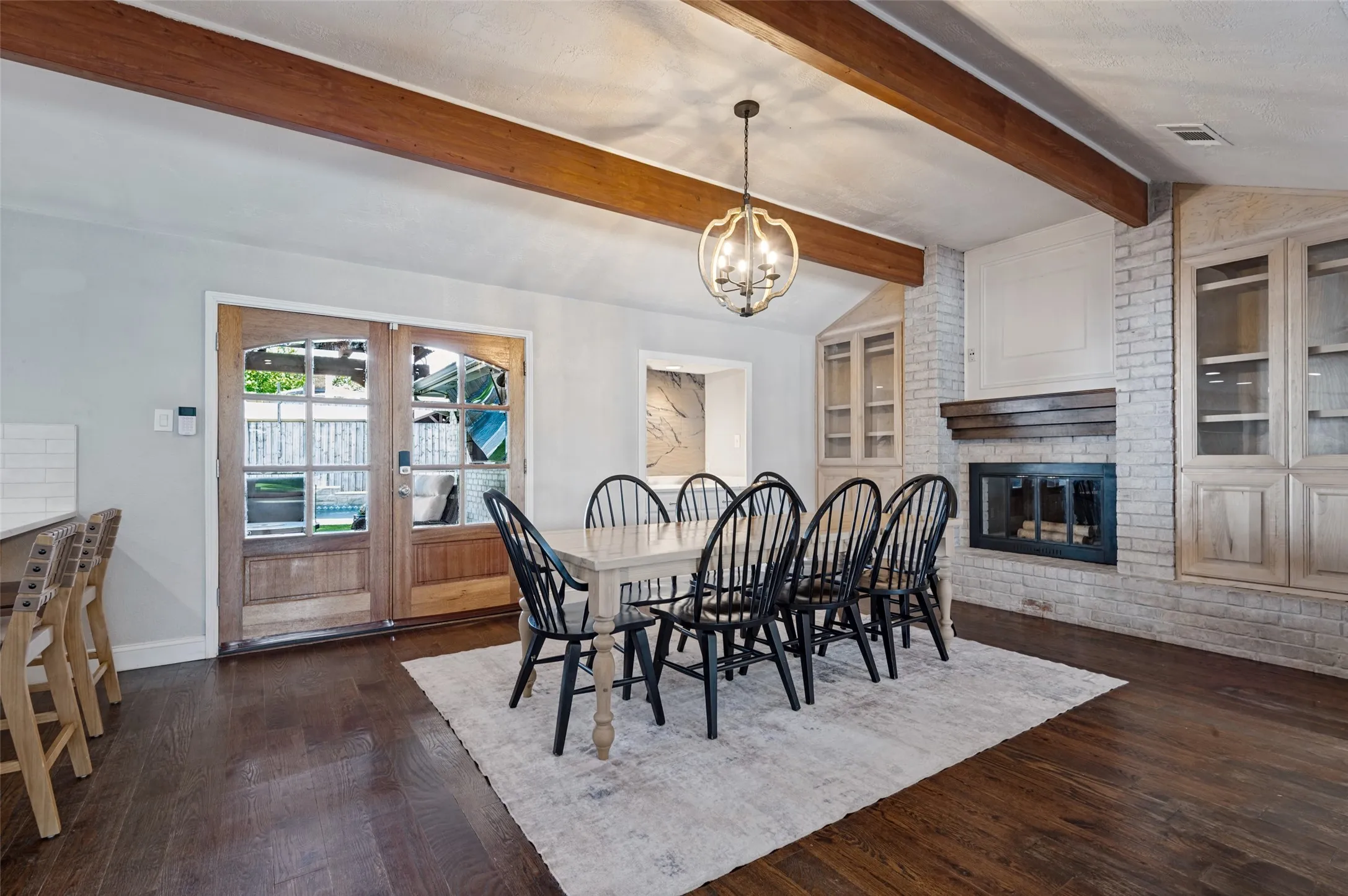 Wood flooring with exposed ceiling beams and a decorative chandelier in dining room, wood burning fire place, custom cabinetry