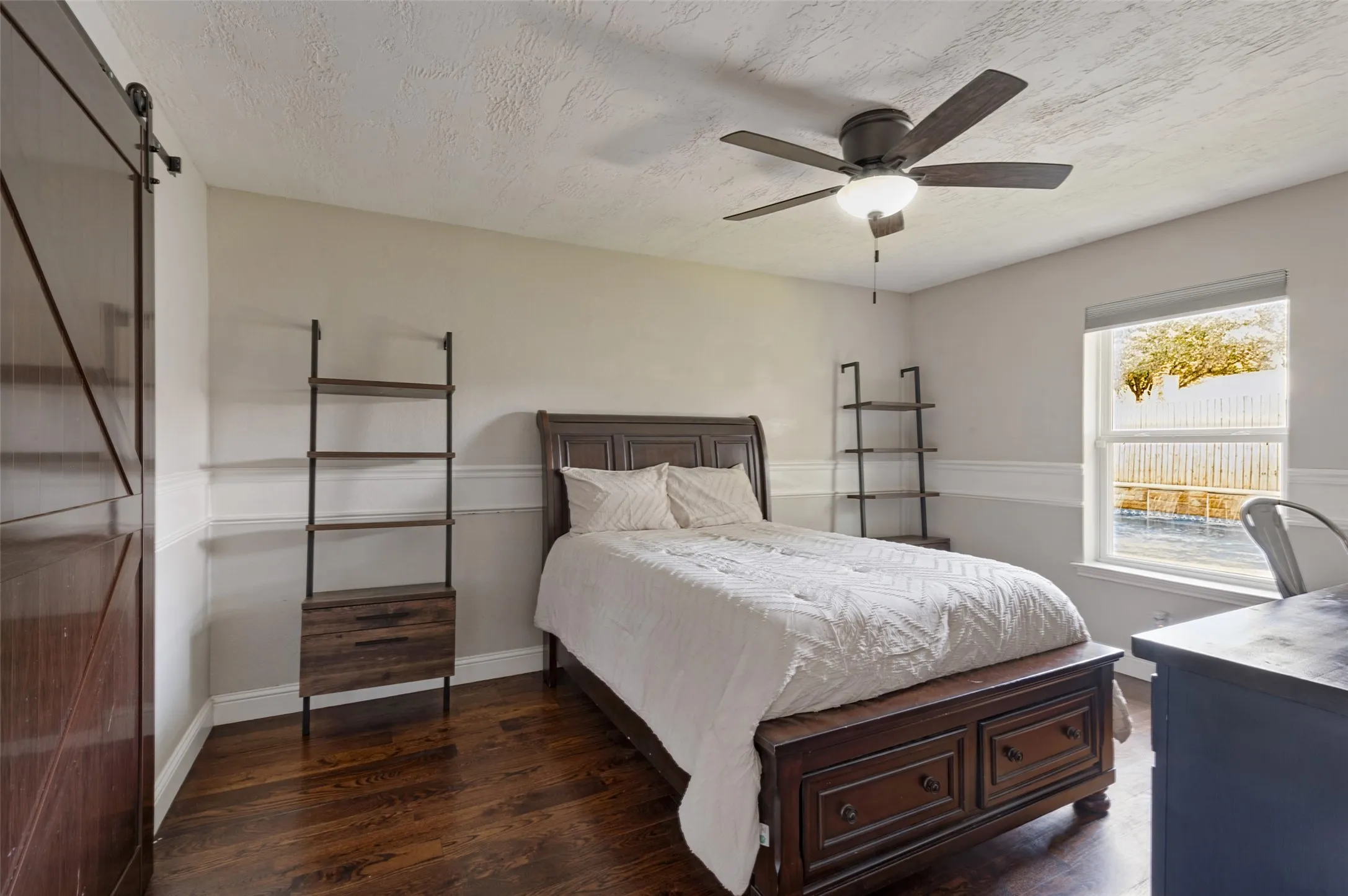 Hardwood flooring, ceiling fan with dark wood-finish barn door in the bedroom