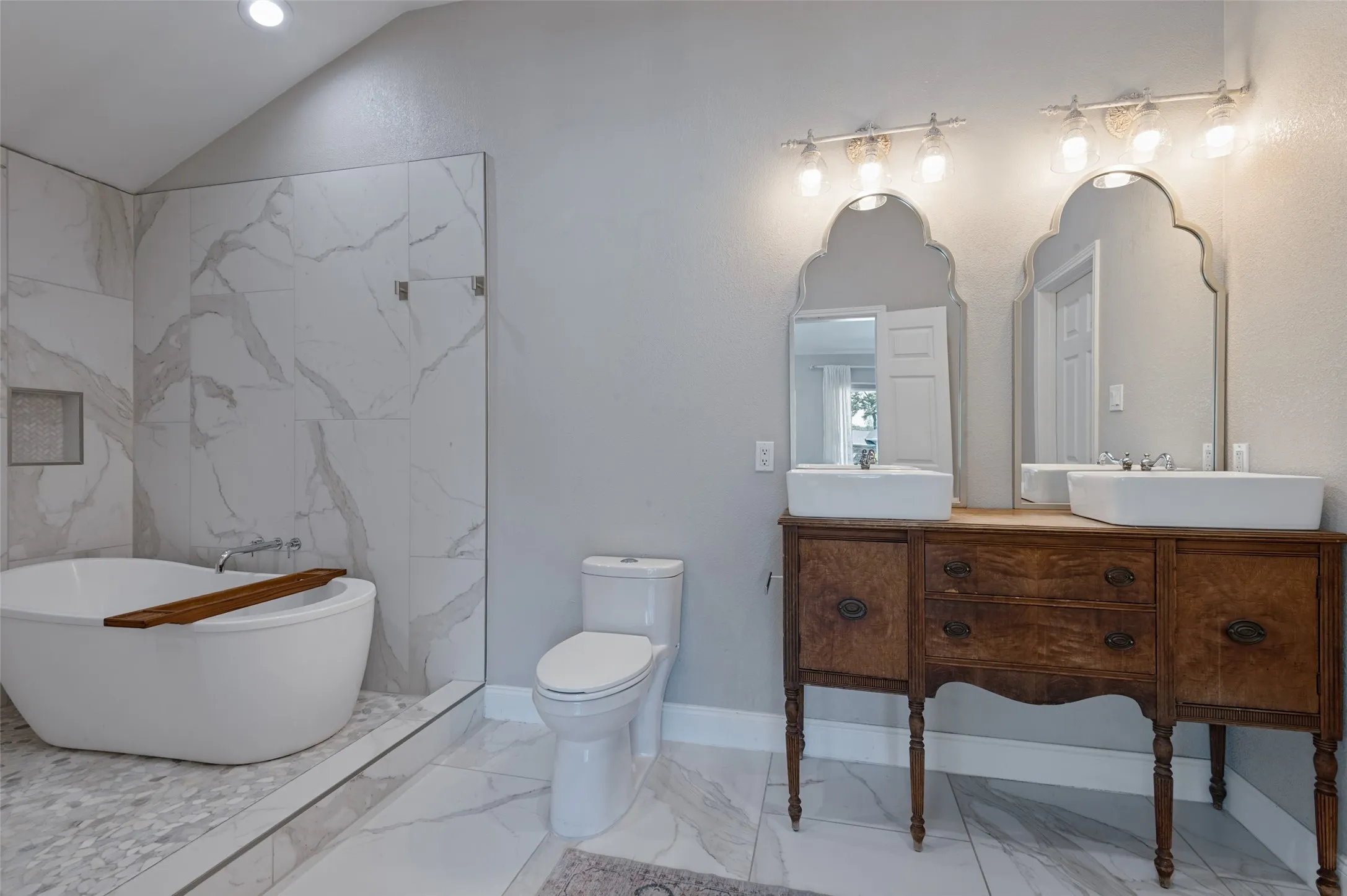 Freestanding bathtub with tile surround, two vessel sinks, and a dual vanity with ornate mirrors in primary bathroom