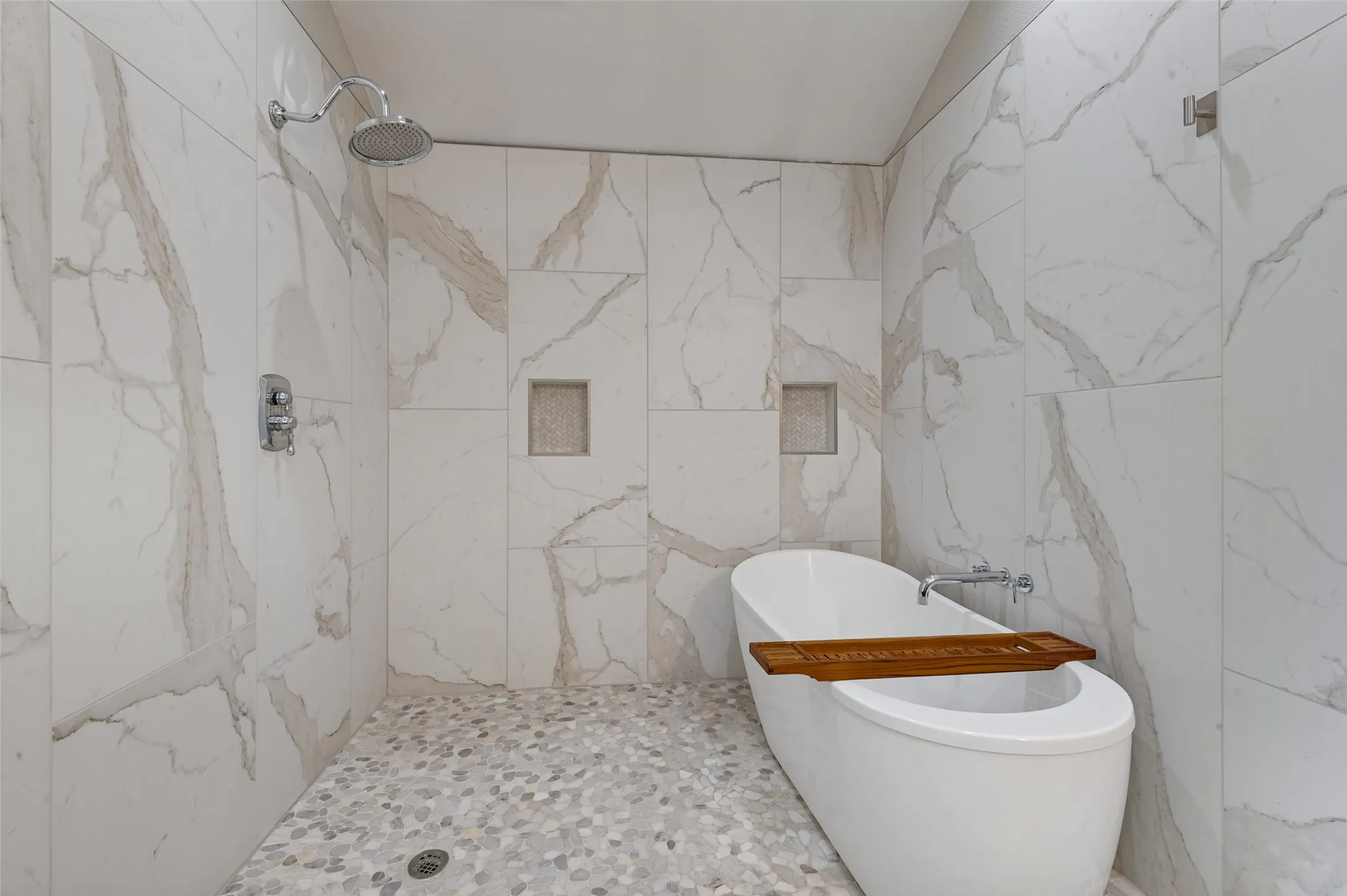 Freestanding soaking tub with chrome fixtures, pebble mosaic shower flooring, and two shower heads included in primary bathroom