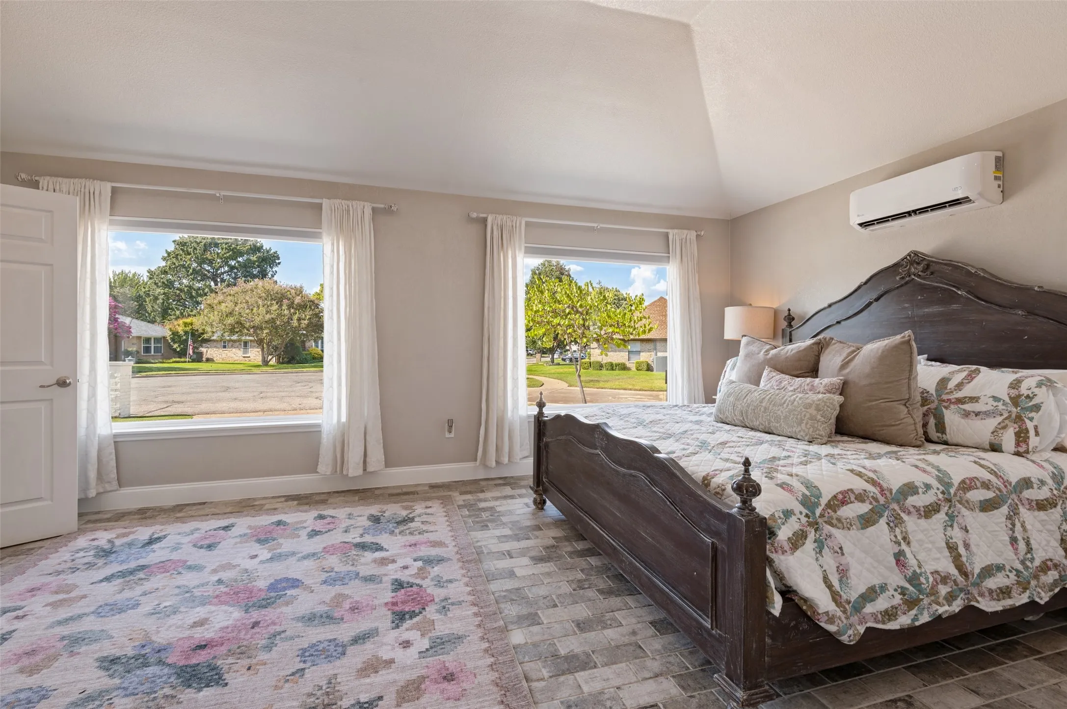 Vaulted ceiling with a mini-split system, two large windows, beautiful flooring in primary bedroom