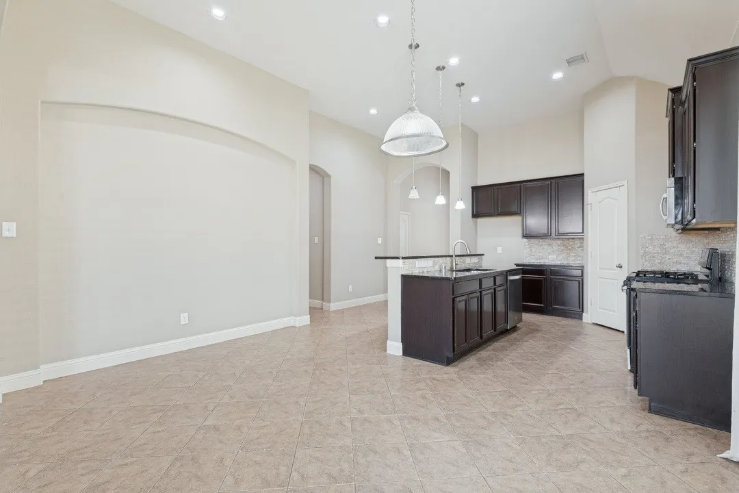 Spacious kitchen with dark wood-finish cabinetry, a large kitchen island with sink, black countertops, and recessed lighting