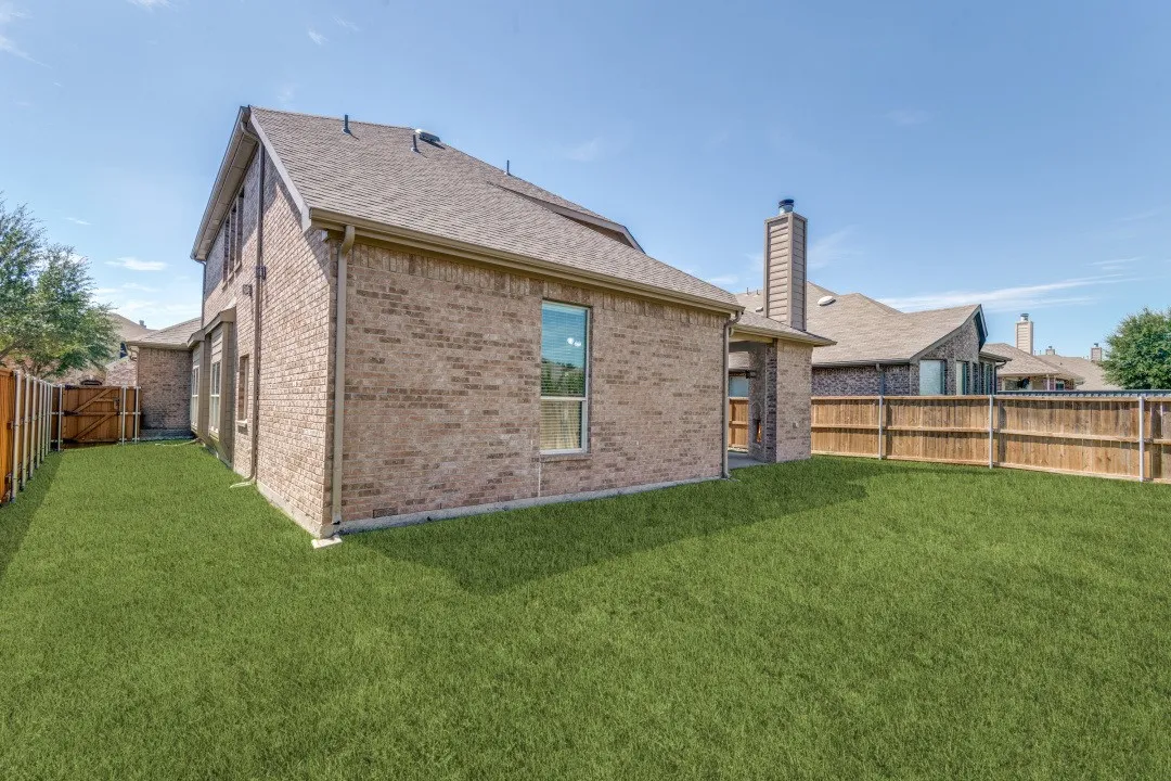 Expansive backyard featuring a manicured lawn, full brick exterior, and a wood privacy fence
