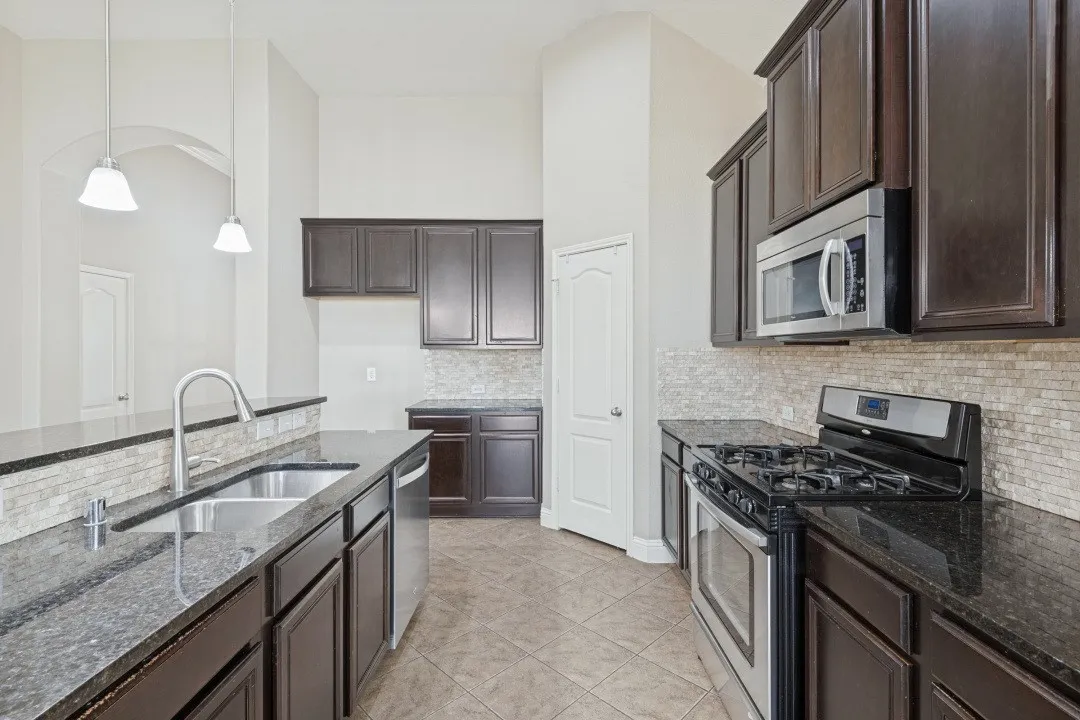 Kitchen featuring dark wood cabinetry, granite countertops, tile backsplash, stainless steel appliances, and a dual basin sink