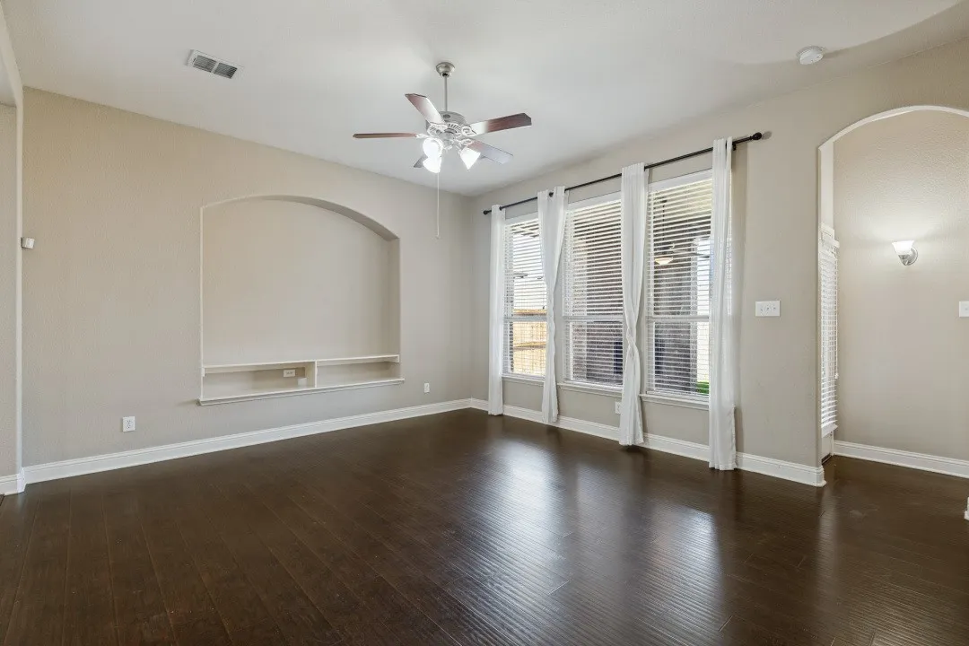 Wood-finish flooring, recessed built-in shelving, arched wall niche, triple windows, and a ceiling fan with integrated lighting  all of this overlooking the rear patio that's covered with an exterior fireplace and ceiling fan