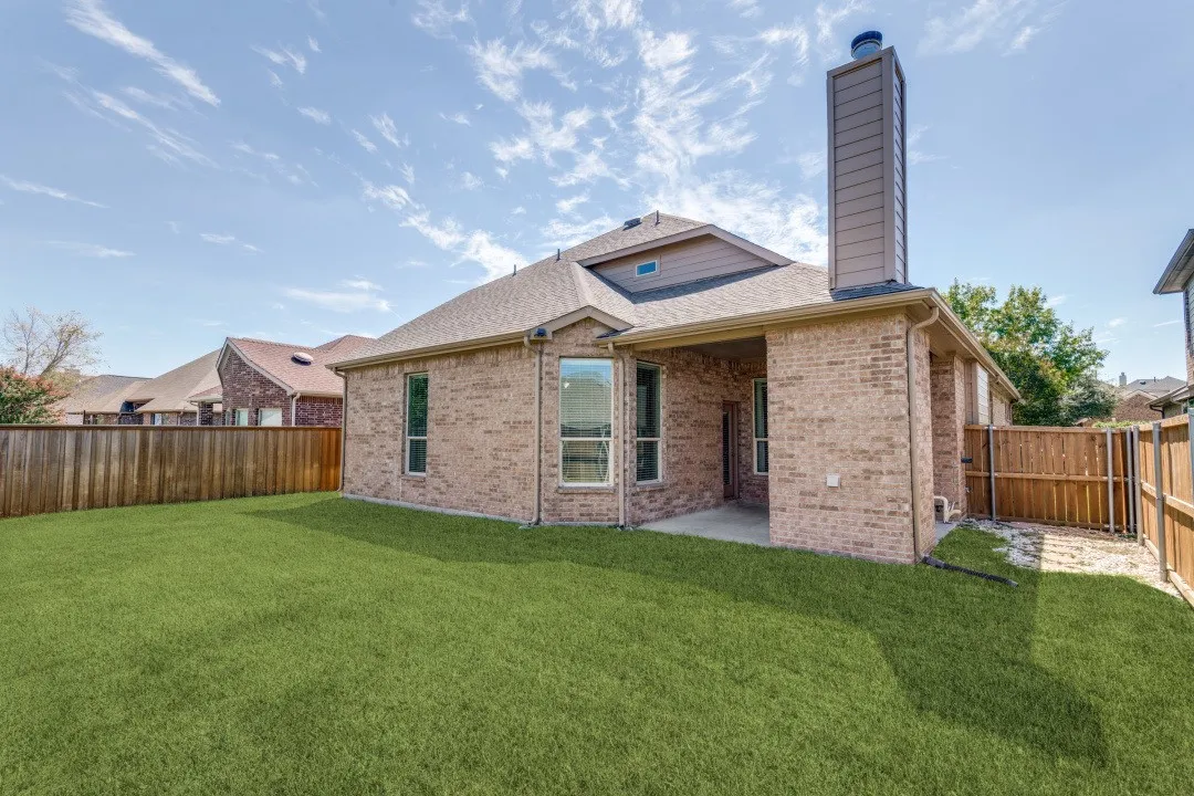 Expansive green lawn, brick exterior, covered patio, privacy fencing, and a prominent chimney