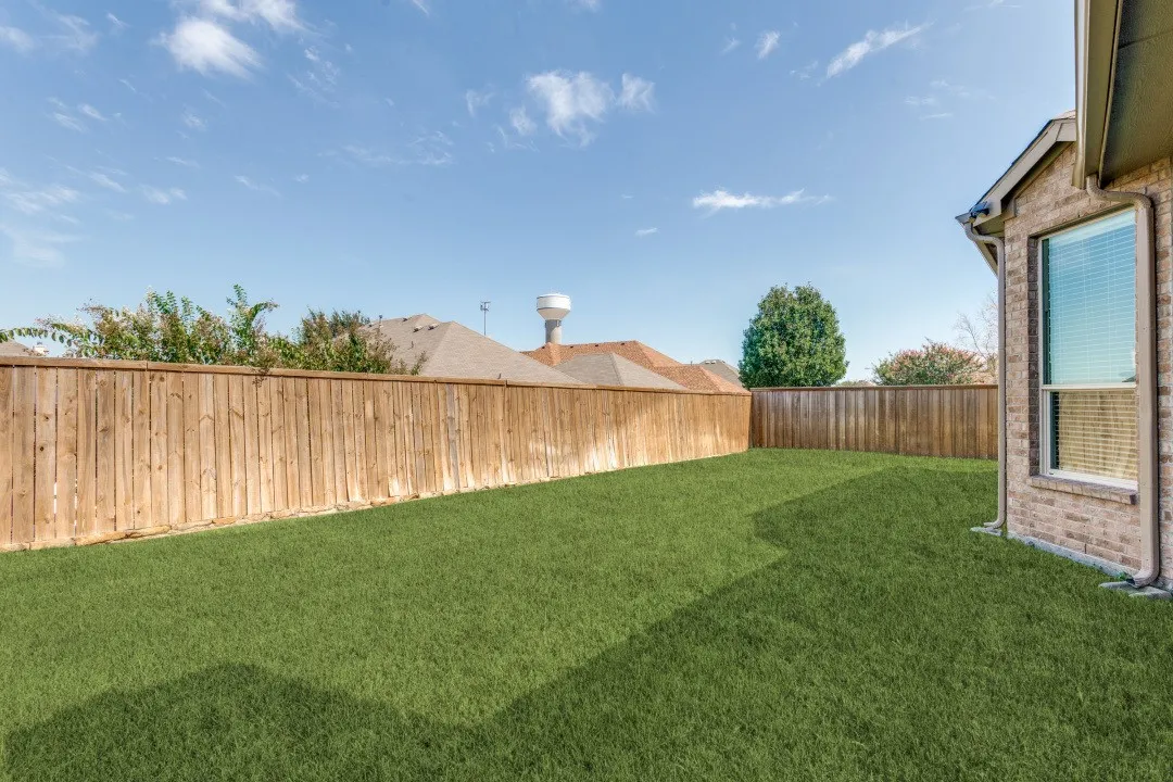 Expansive backyard featuring a manicured lawn, full wood privacy fencing, and a brick exterior wall with a large window