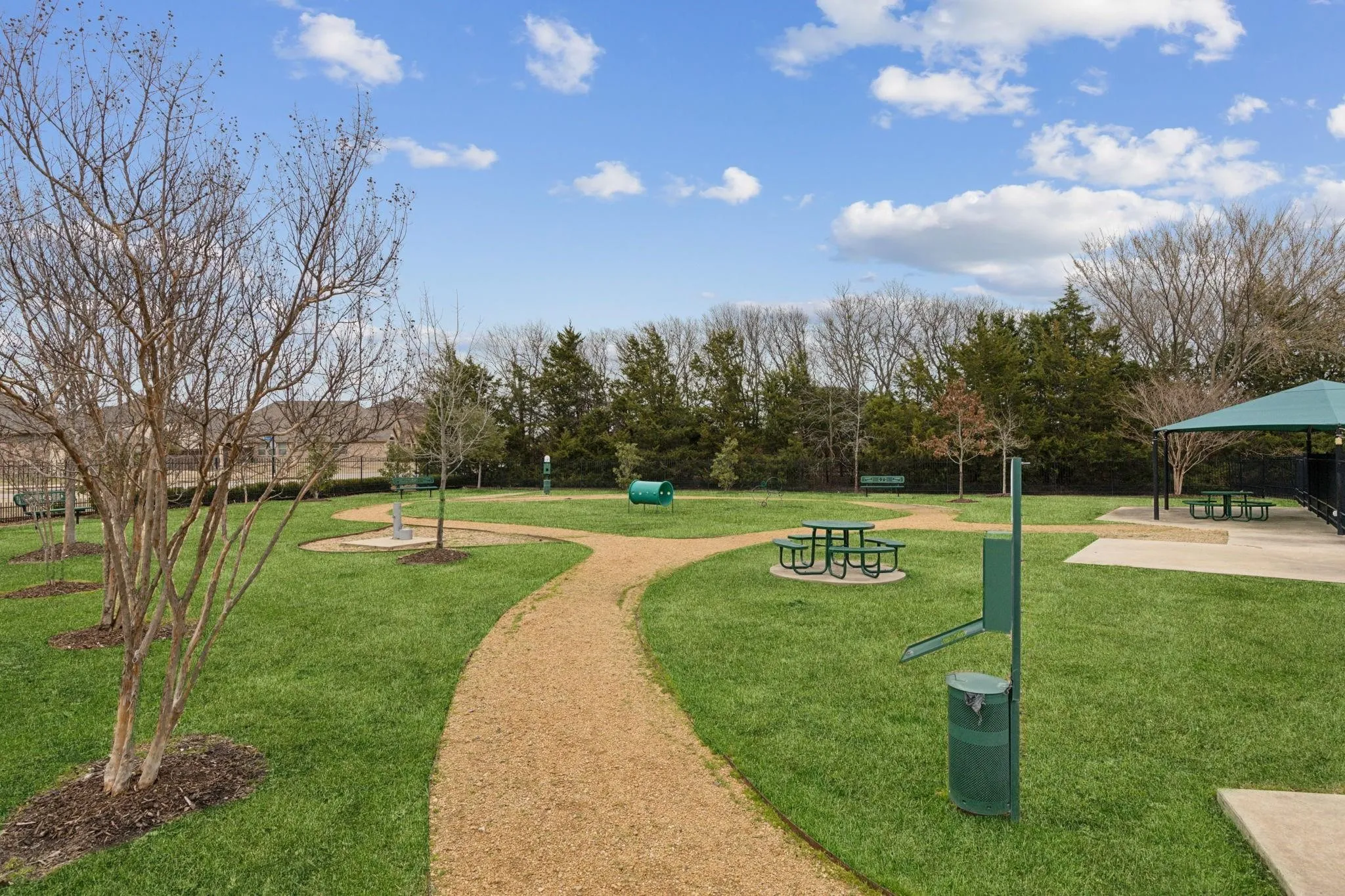 Expansive green space featuring a gravel walking path, picnic tables, covered pavilion, and dedicated pet amenities