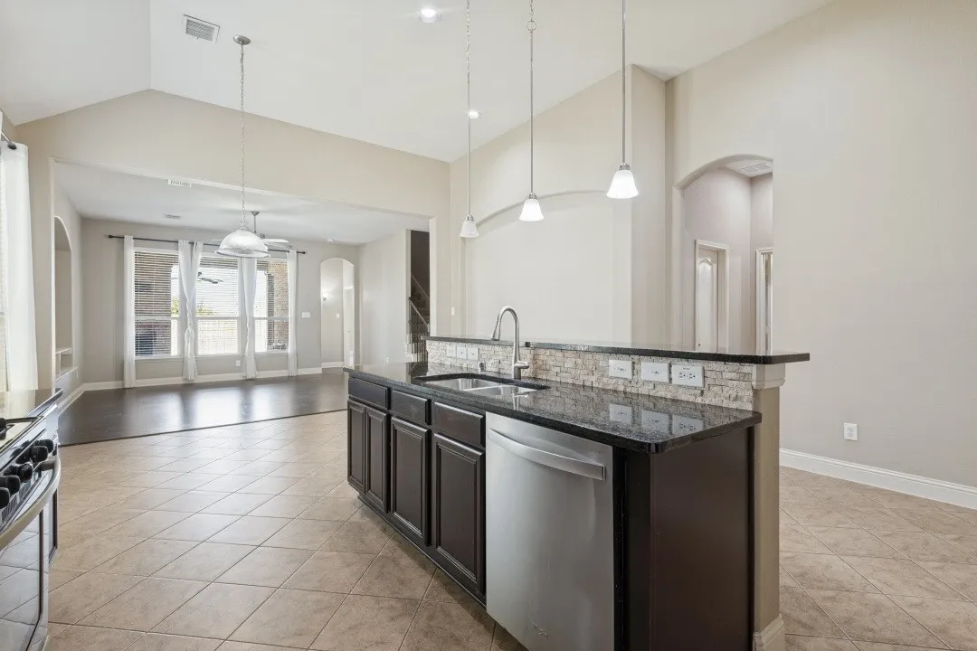 Kitchen island with a dark countertop and built-in stainless steel dishwasher, tile flooring, vaulted ceiling, recessed lighting, and arched doorways