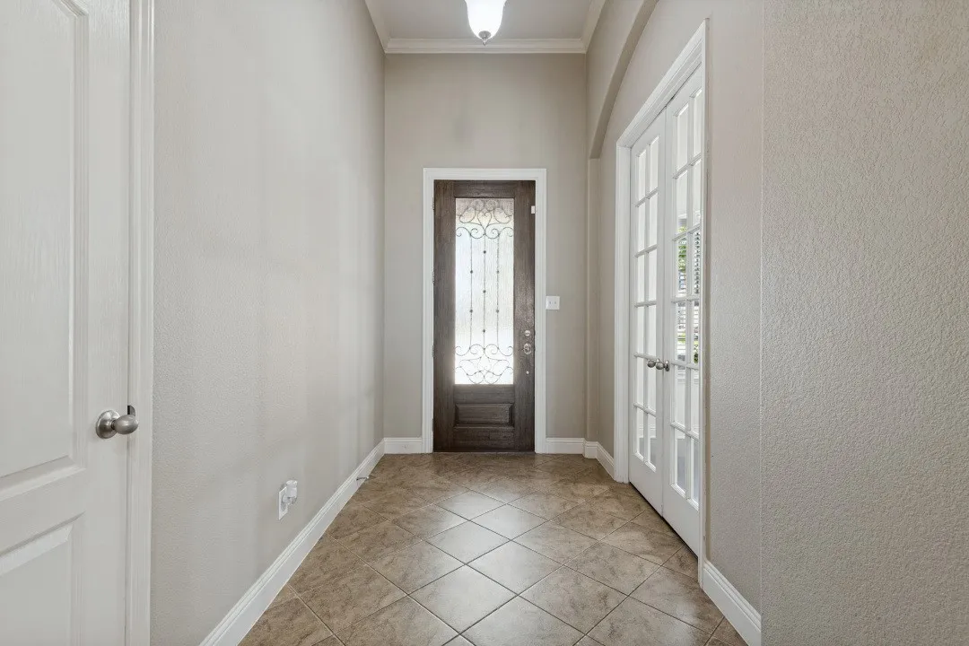Entryway featuring diagonal tile flooring, a dark wood entry door with ornate glass, white French doors, and crown molding
