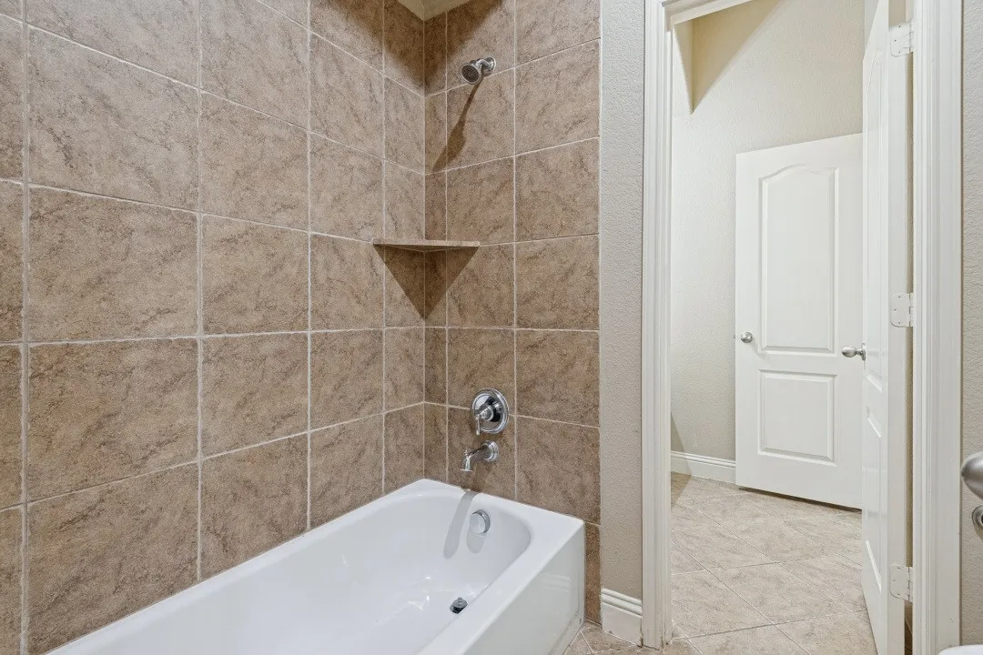 Bathtub with tile surround, built-in corner shelf, and polished chrome fixtures