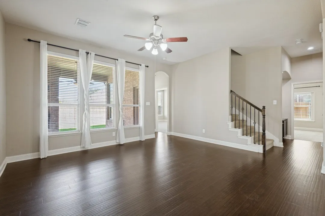 Expansive main living area featuring dark wood-finish flooring, a ceiling fan with light kit, and multiple large windows