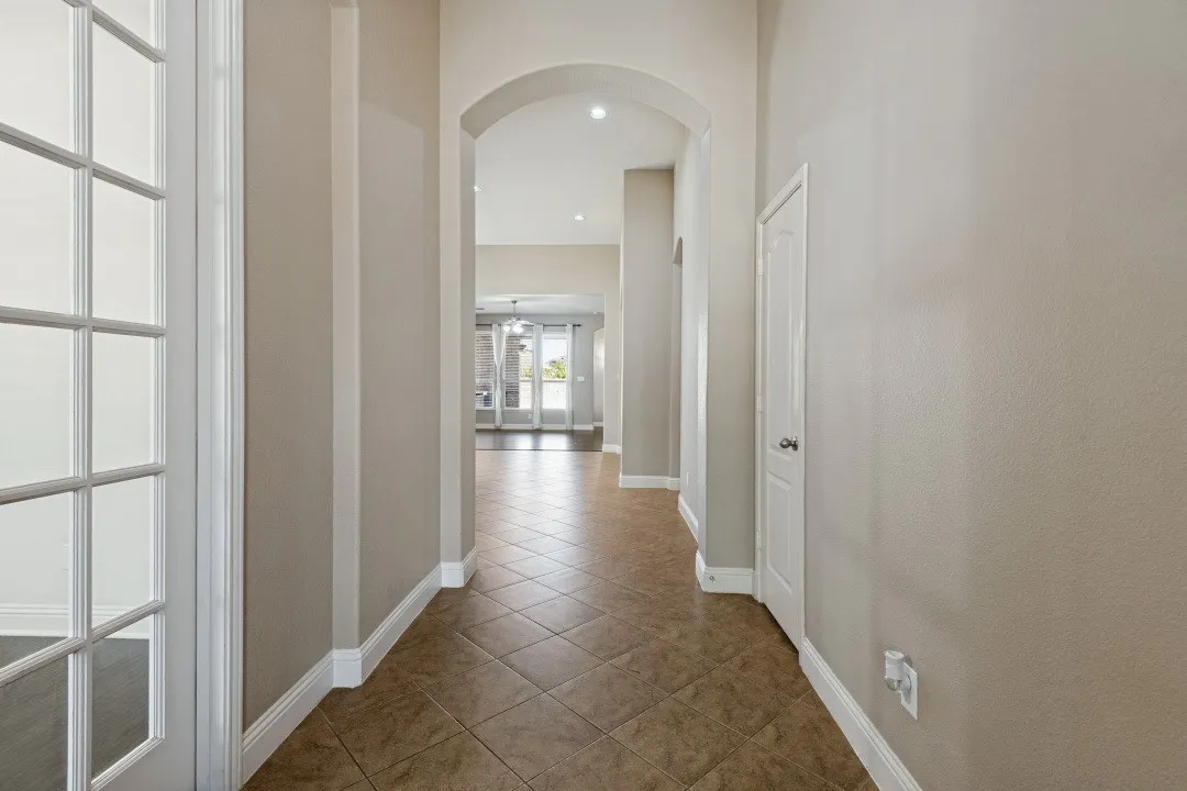 Hallway with diagonally laid tile flooring, arched entryway, and white trim