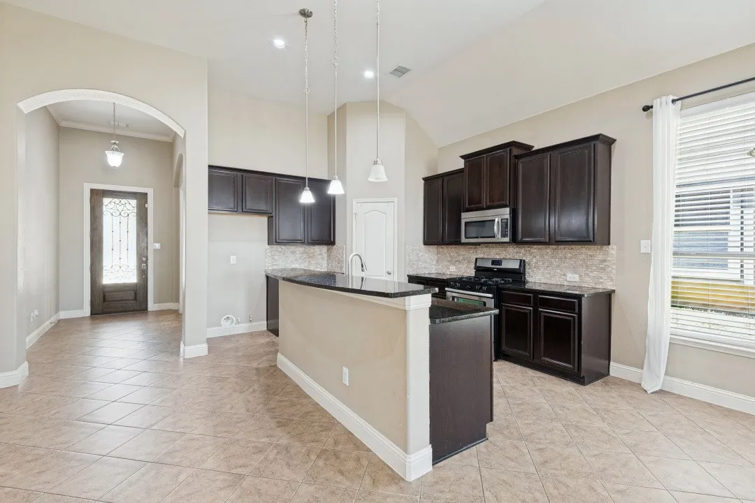 Kitchen featuring dark wood cabinetry, stainless steel microwave, gas range, and stone countertops
