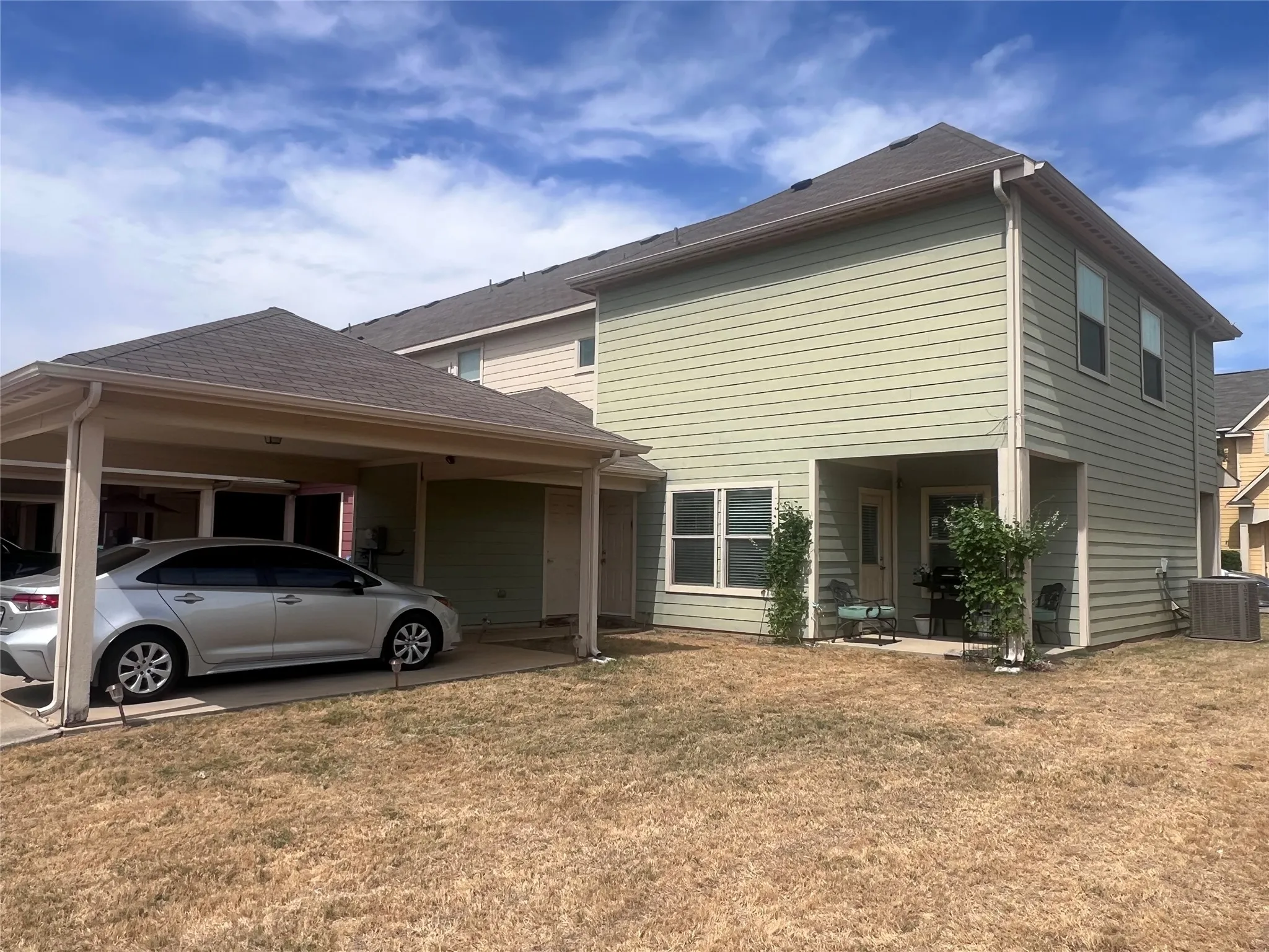Two-story exterior with light green siding, covered carport, and covered patio area