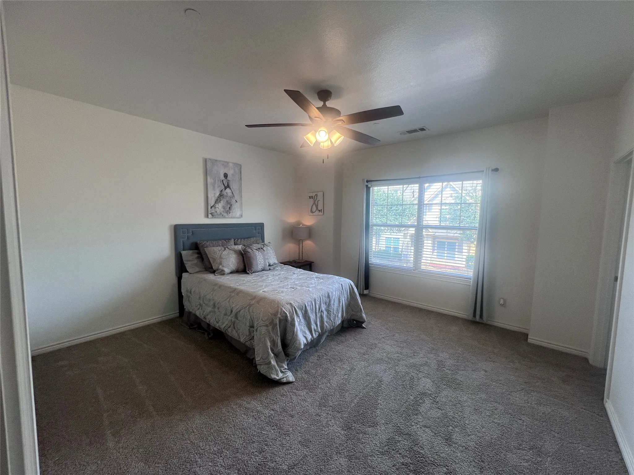 Spacious room with large window, ceiling fan, and neutral-toned carpeting