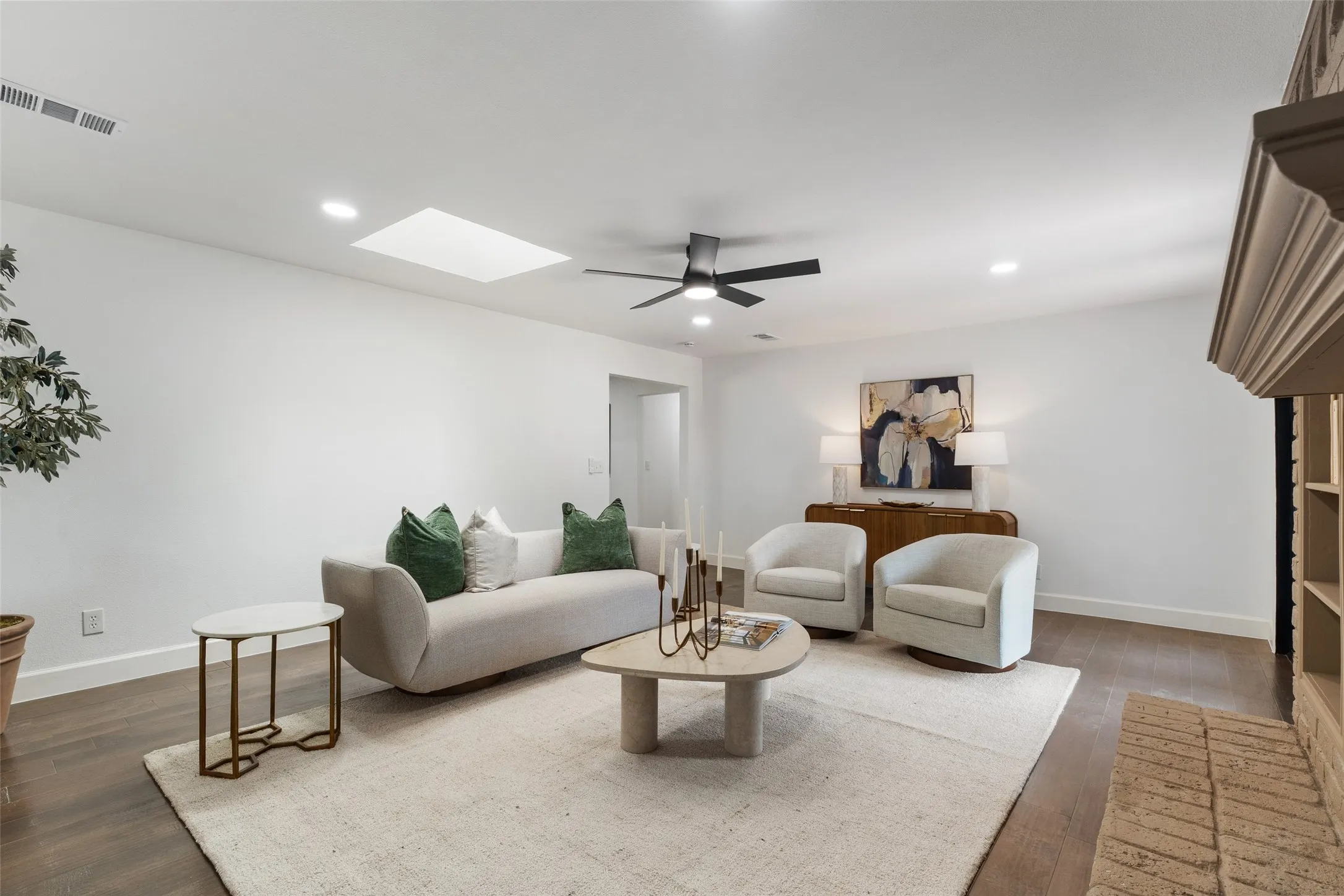Recessed lighting, wood-finish flooring, a ceiling fan, and a skylight illuminate this living space