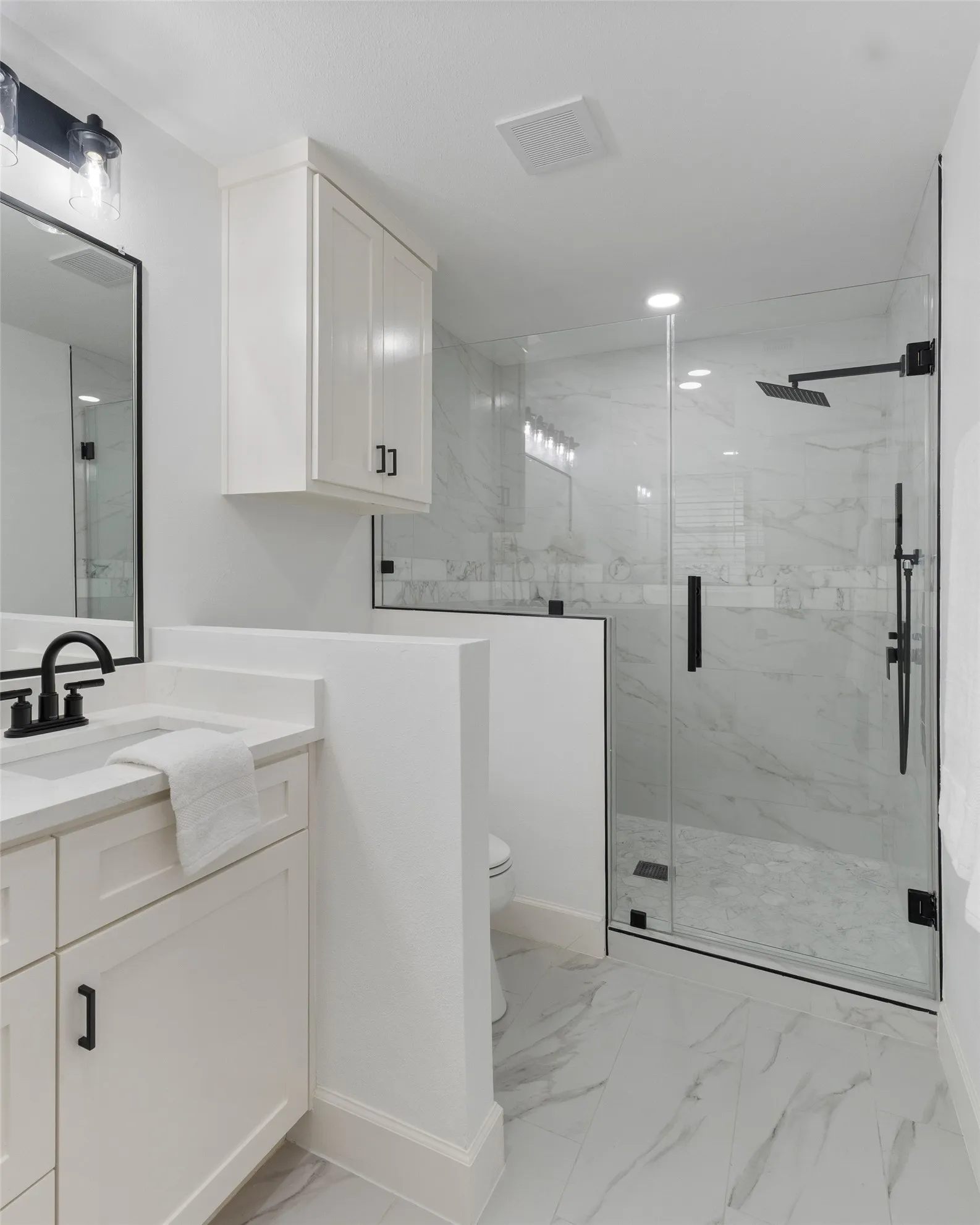 Bathroom featuring a glass-enclosed shower with black fixtures, white vanity with integrated sink, white upper cabinetry, and large format tile flooring