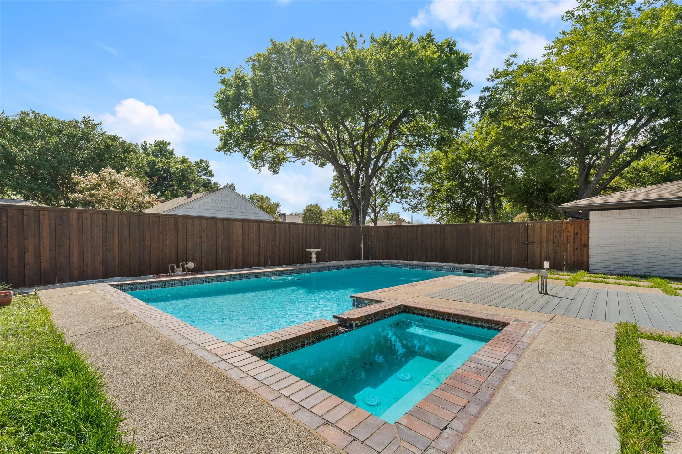 Swimming pool with an integrated hot tub, surrounded by exposed aggregate concrete decking and brick coping