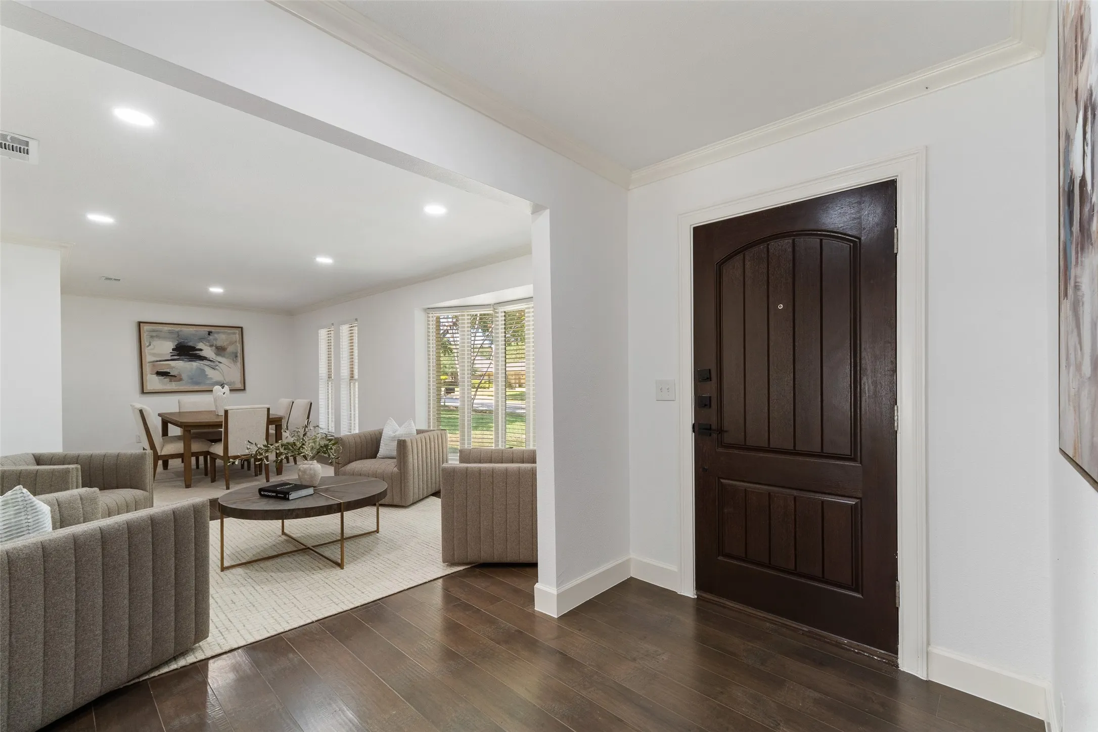 Dark wood-finish entry door, wide plank wood-finish flooring, recessed ceiling lighting, and a bay window