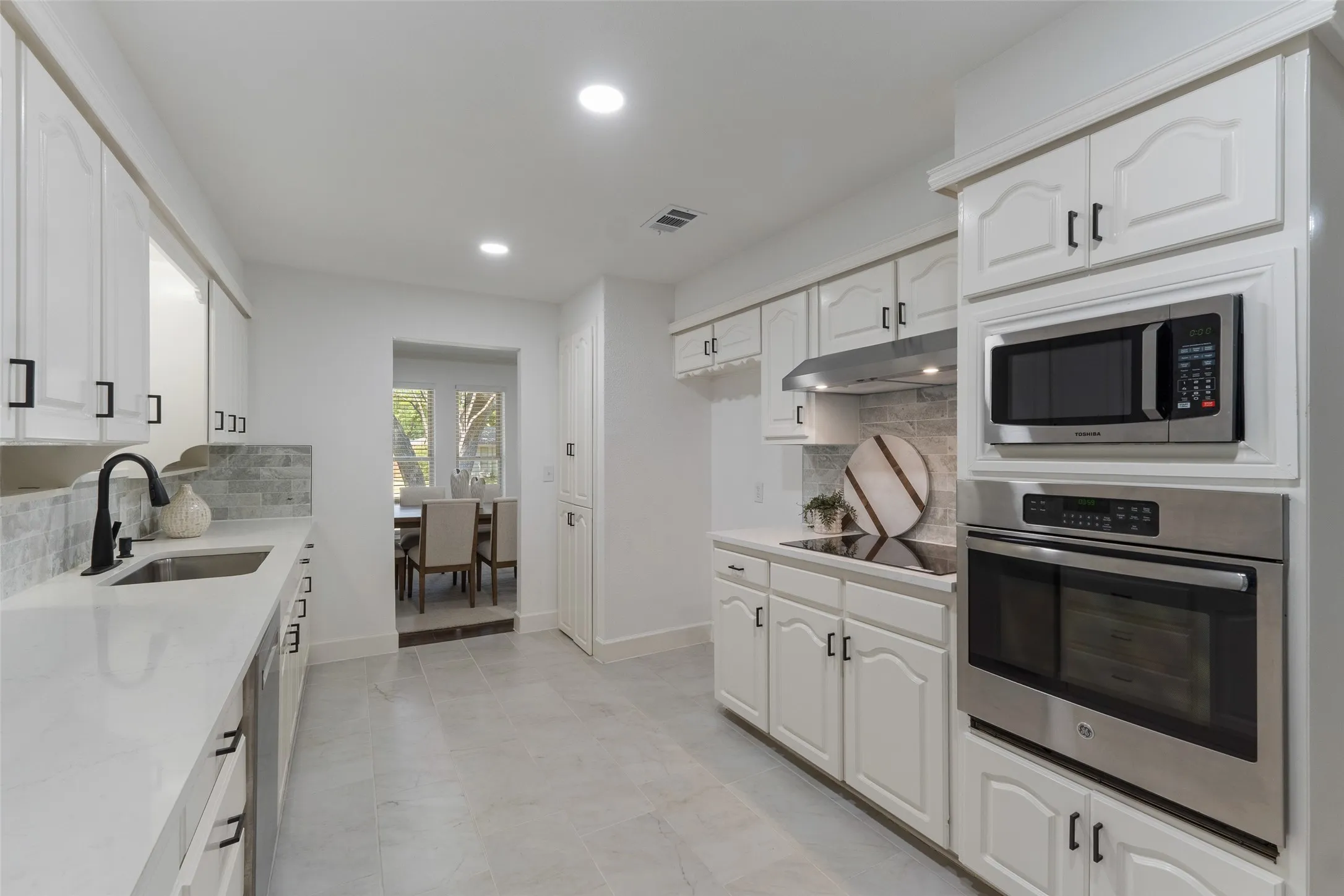 Kitchen featuring white cabinetry, integrated stainless steel appliances, light-toned countertops, and a tiled backsplash