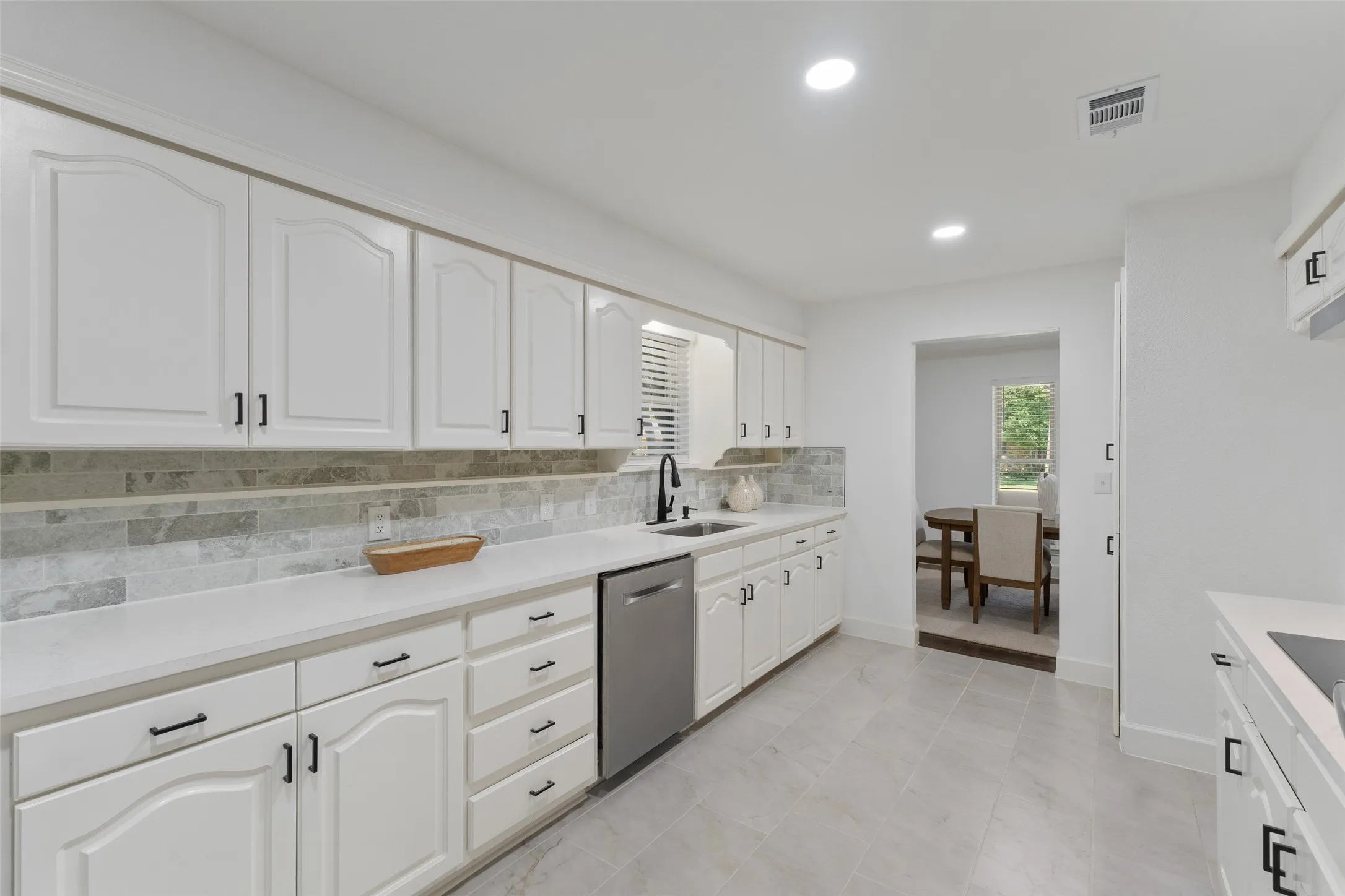 White cabinetry with black hardware, light-toned countertops, a light-toned tile backsplash, and stainless steel appliances
