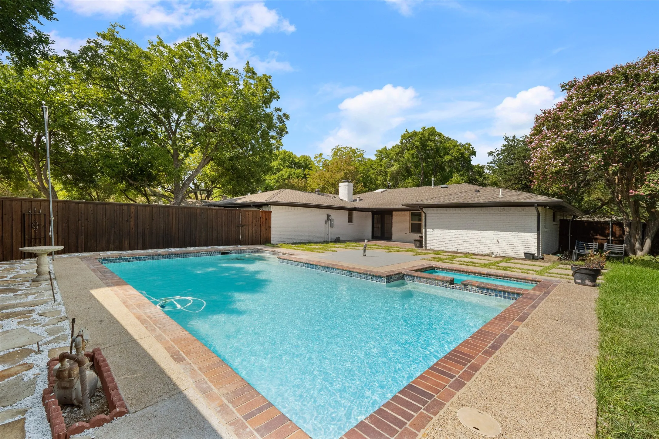 Backyard features an in-ground swimming pool with an integrated spa, brick coping, and a surrounding concrete deck