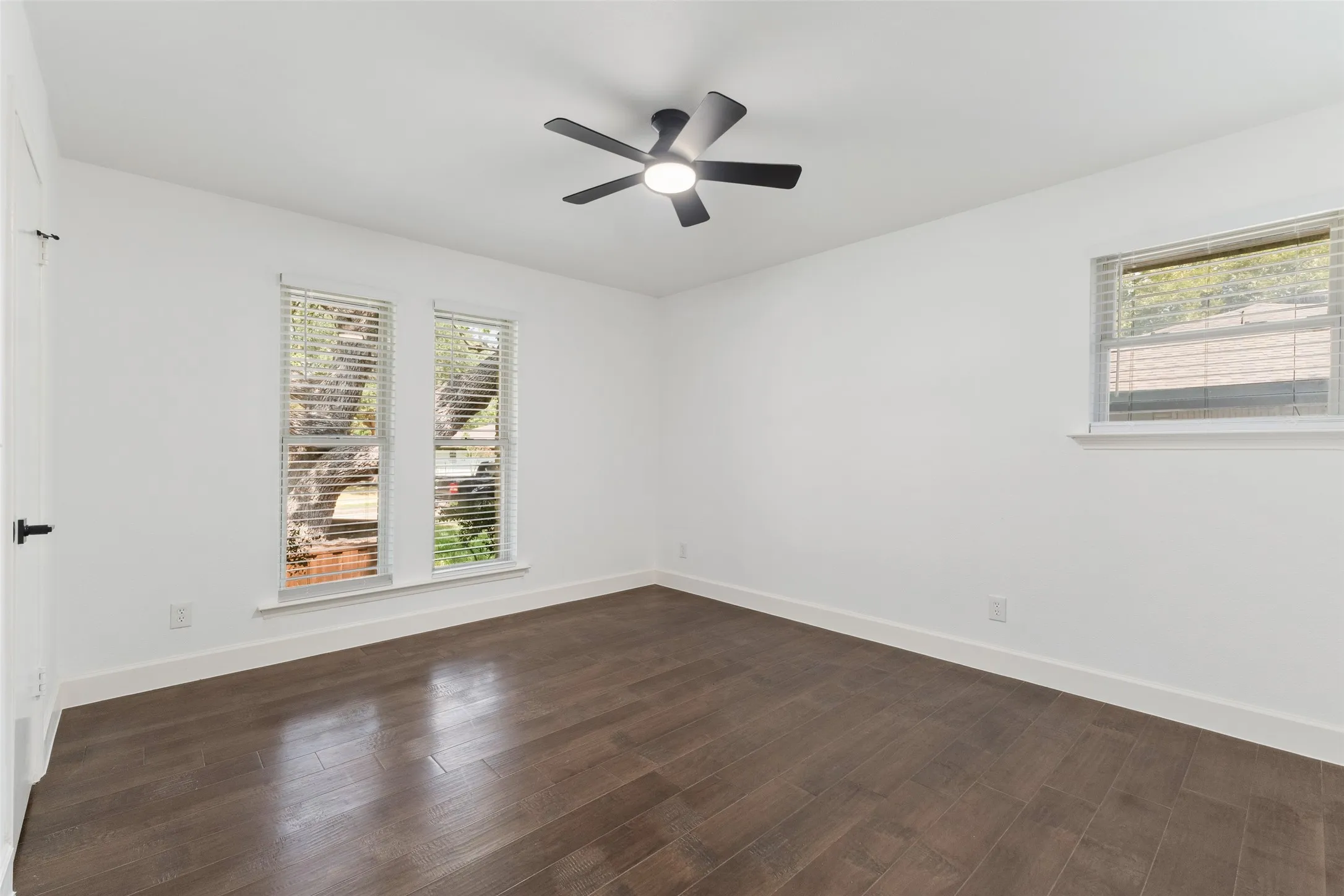 Smooth white walls, dark wood-finish flooring, and a modern ceiling fan with integrated lighting