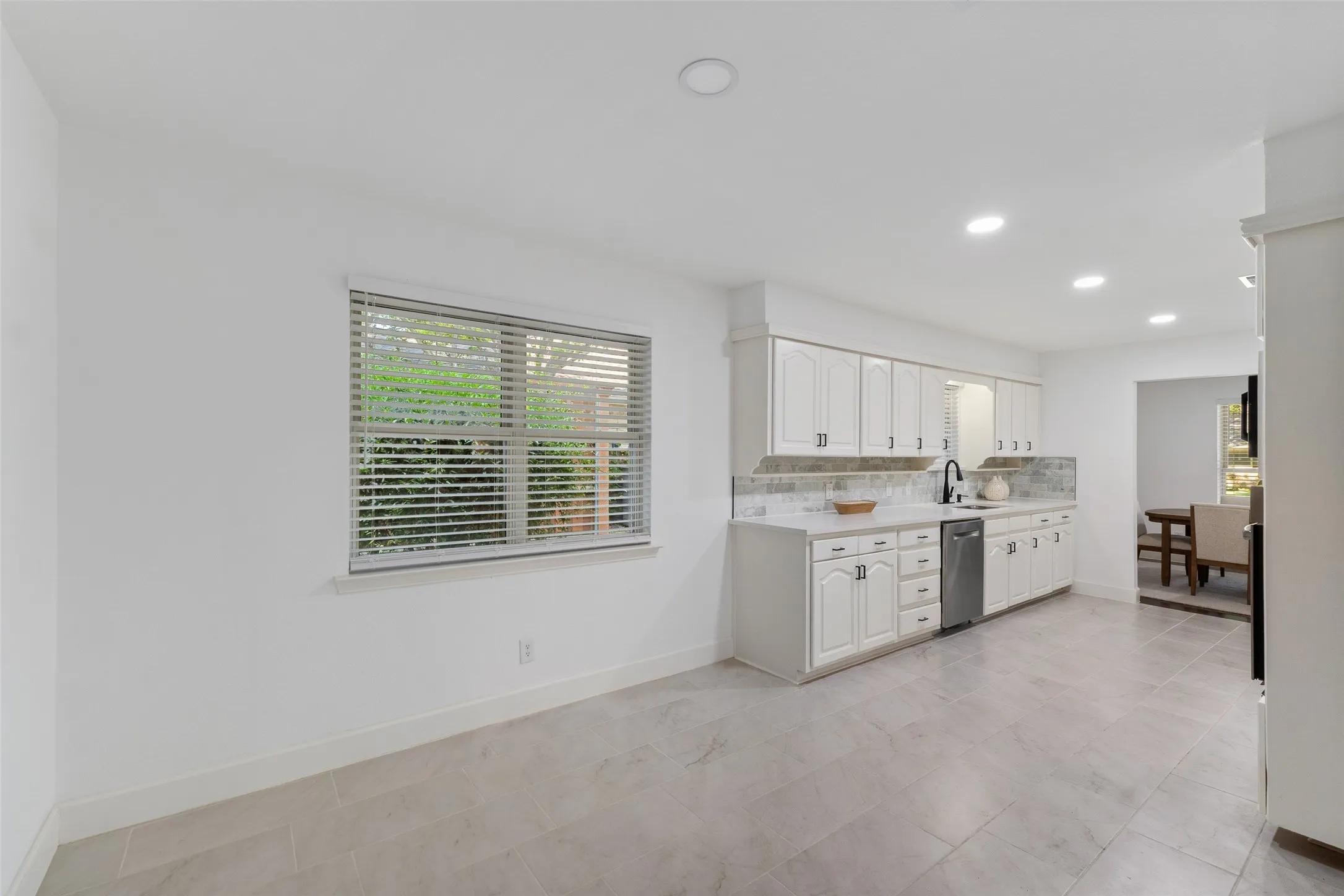 Kitchen featuring white shaker-style cabinetry, light-toned countertops, stone-look backsplash, and recessed lighting
