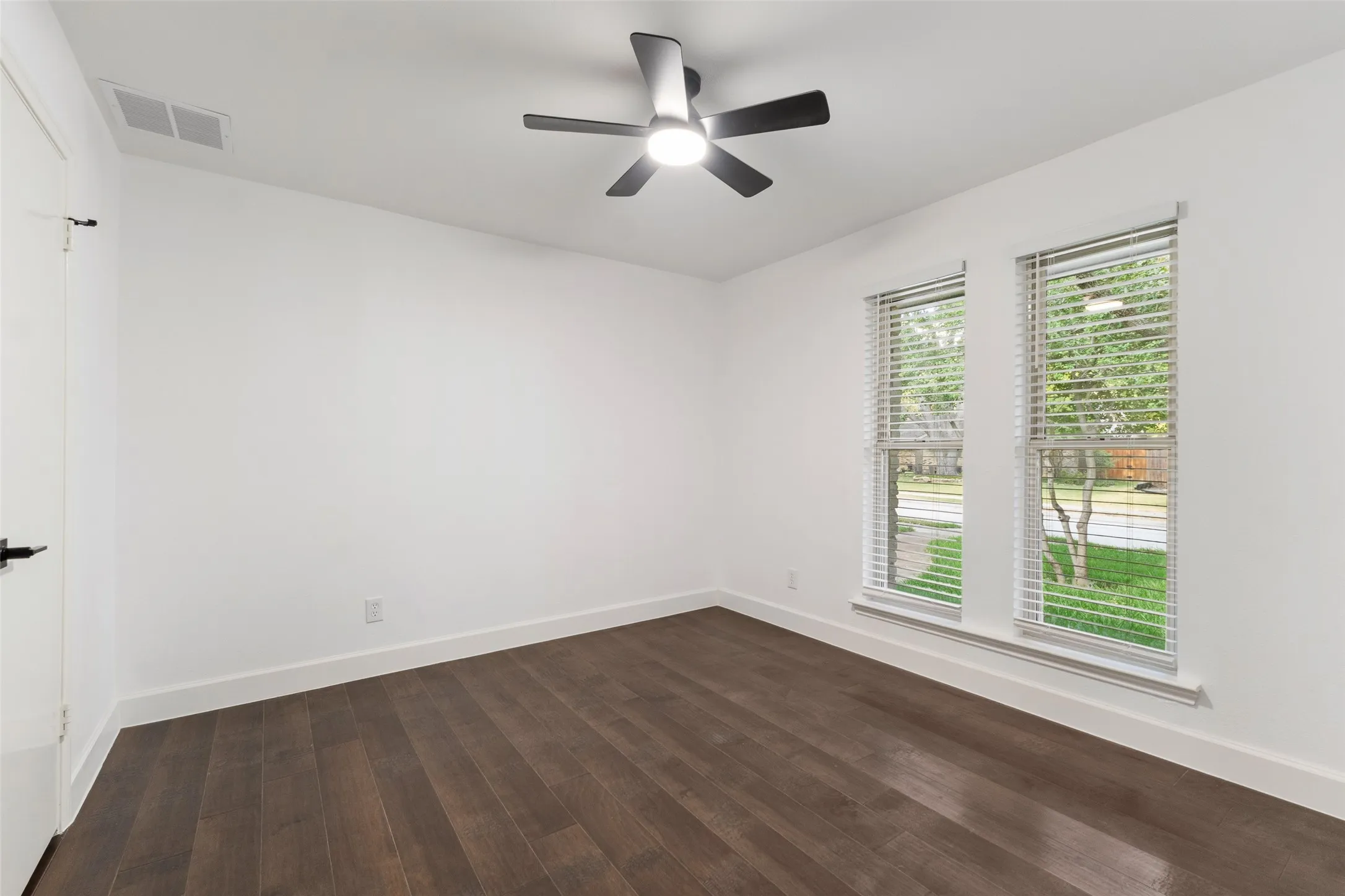 Wood-finish flooring, dual windows with blinds, and a ceiling fan with integrated lighting