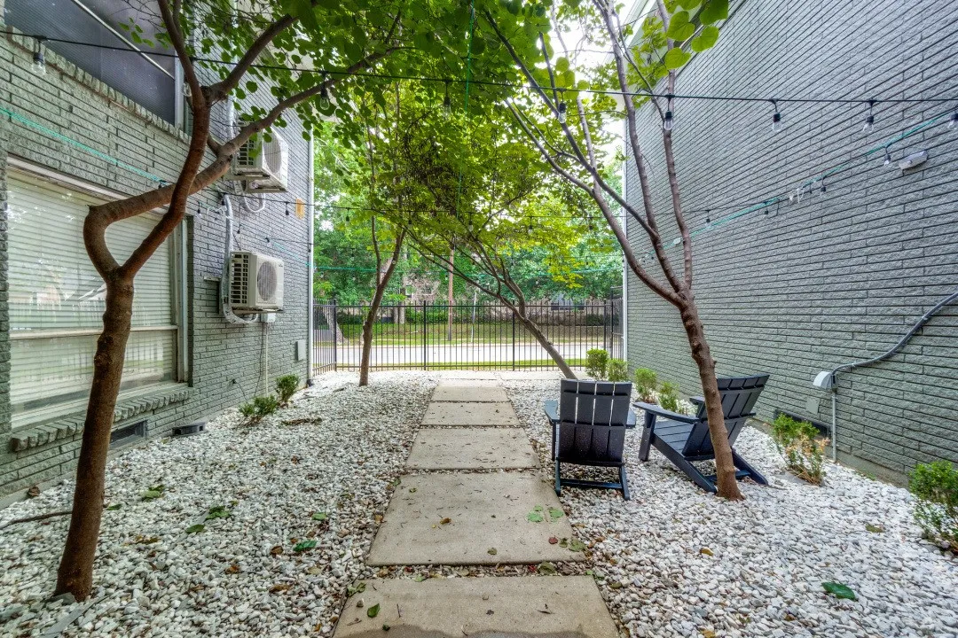 Outdoor patio area featuring a concrete paver walkway, white decorative gravel, and mature trees