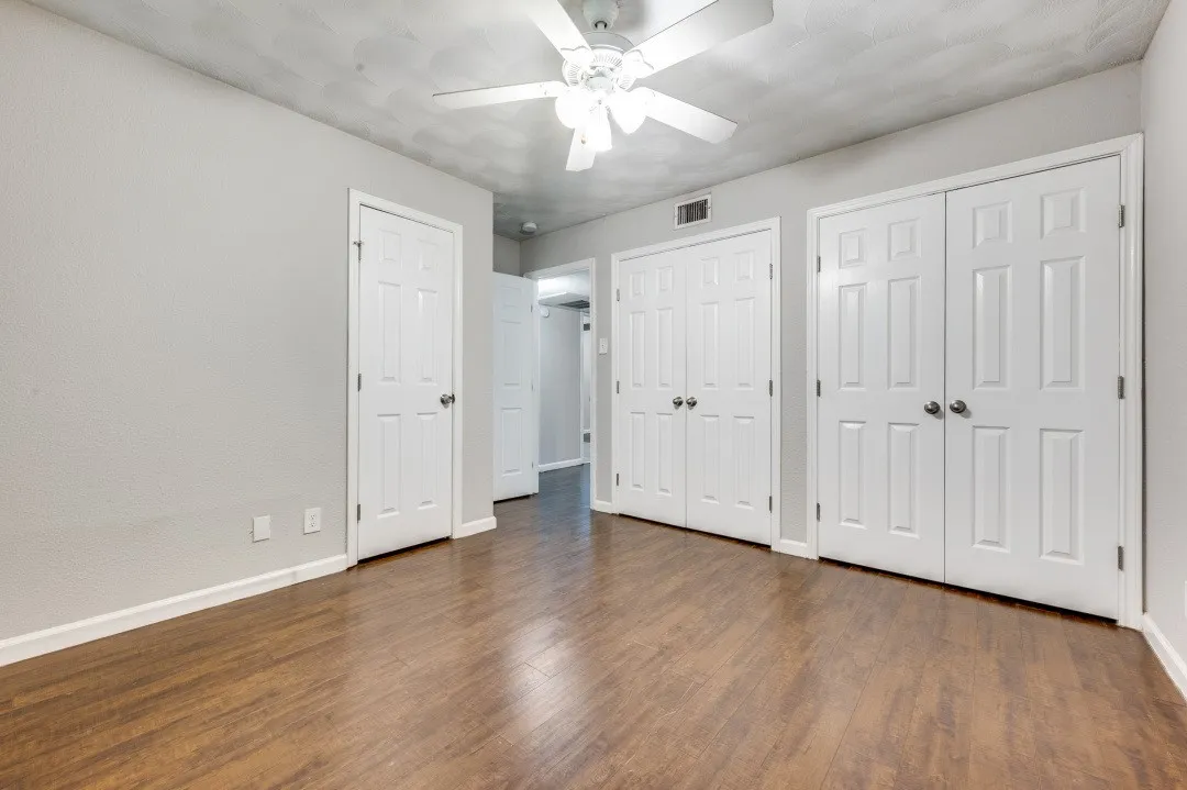 Wood-finish flooring with white baseboards, a ceiling fan, and multiple paneled doors