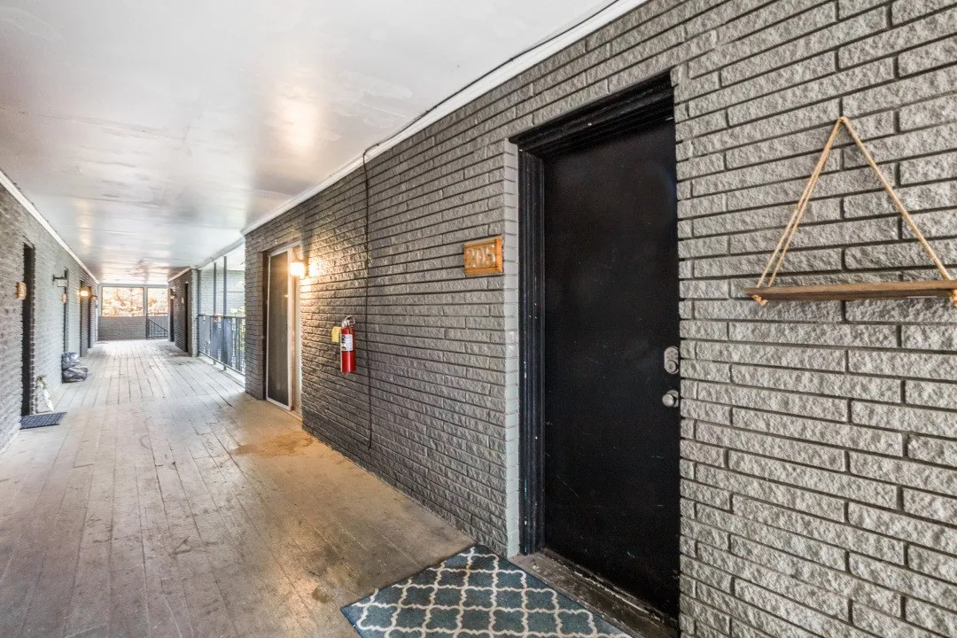 Hallway featuring brick-patterned walls, wood-finish flooring, and wall-mounted lighting