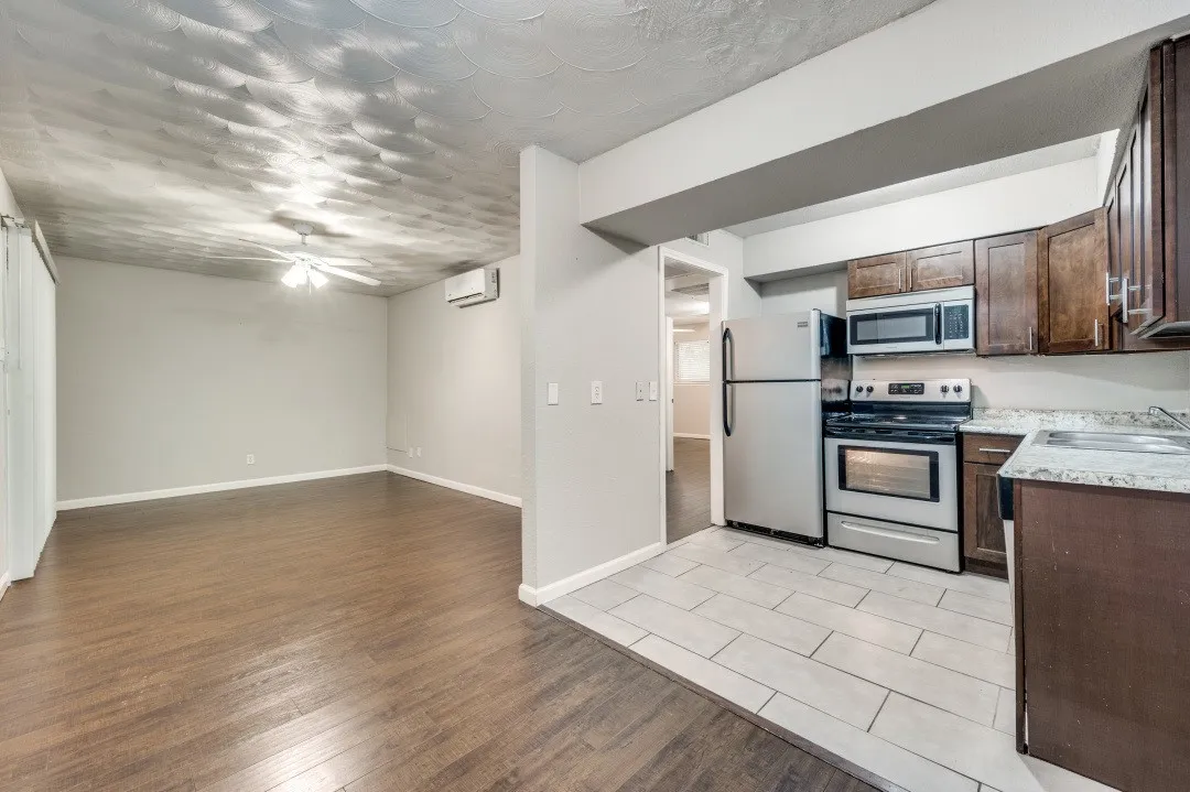 Integrated living and kitchen area featuring wood-finish flooring, a ceiling fan, and a wall-mounted air conditioning unit