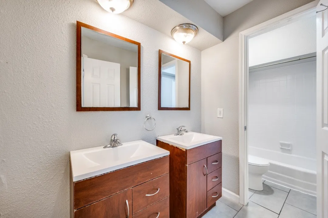 Dual vanities with wood-finish cabinetry, chrome fixtures, and individual wall mirrors
