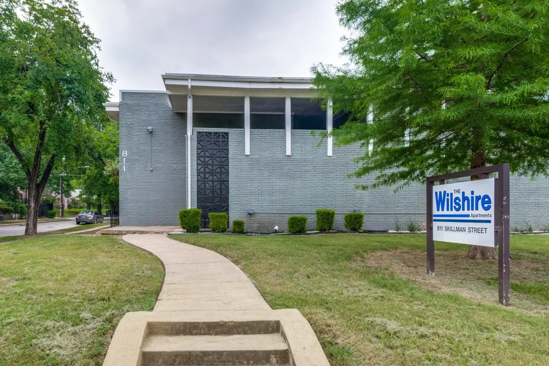 Building exterior with textured gray brick, concrete walkway, and established landscaping